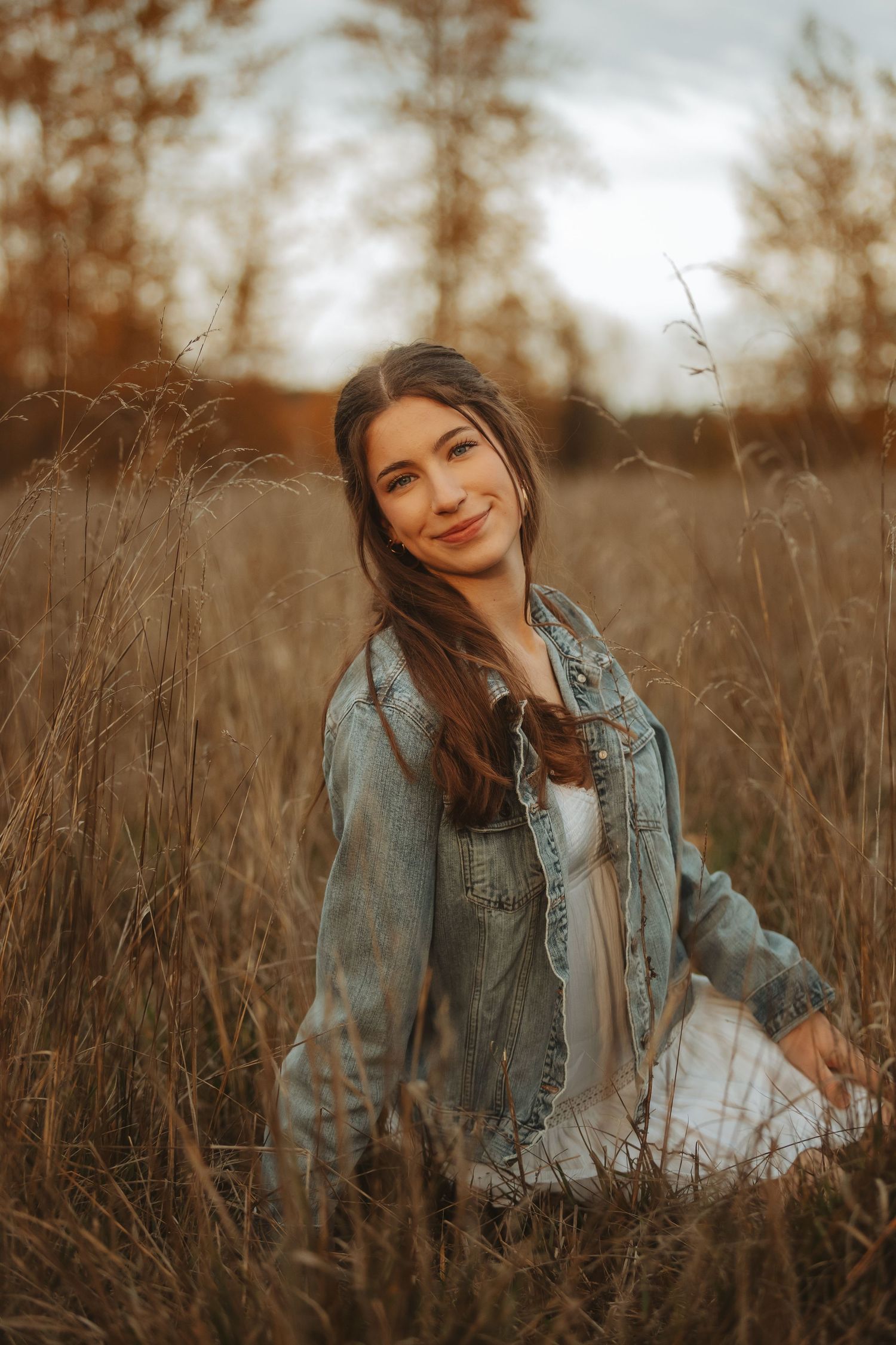 Portrait in autumn field wearing denim jacket among tall grass during sunset.