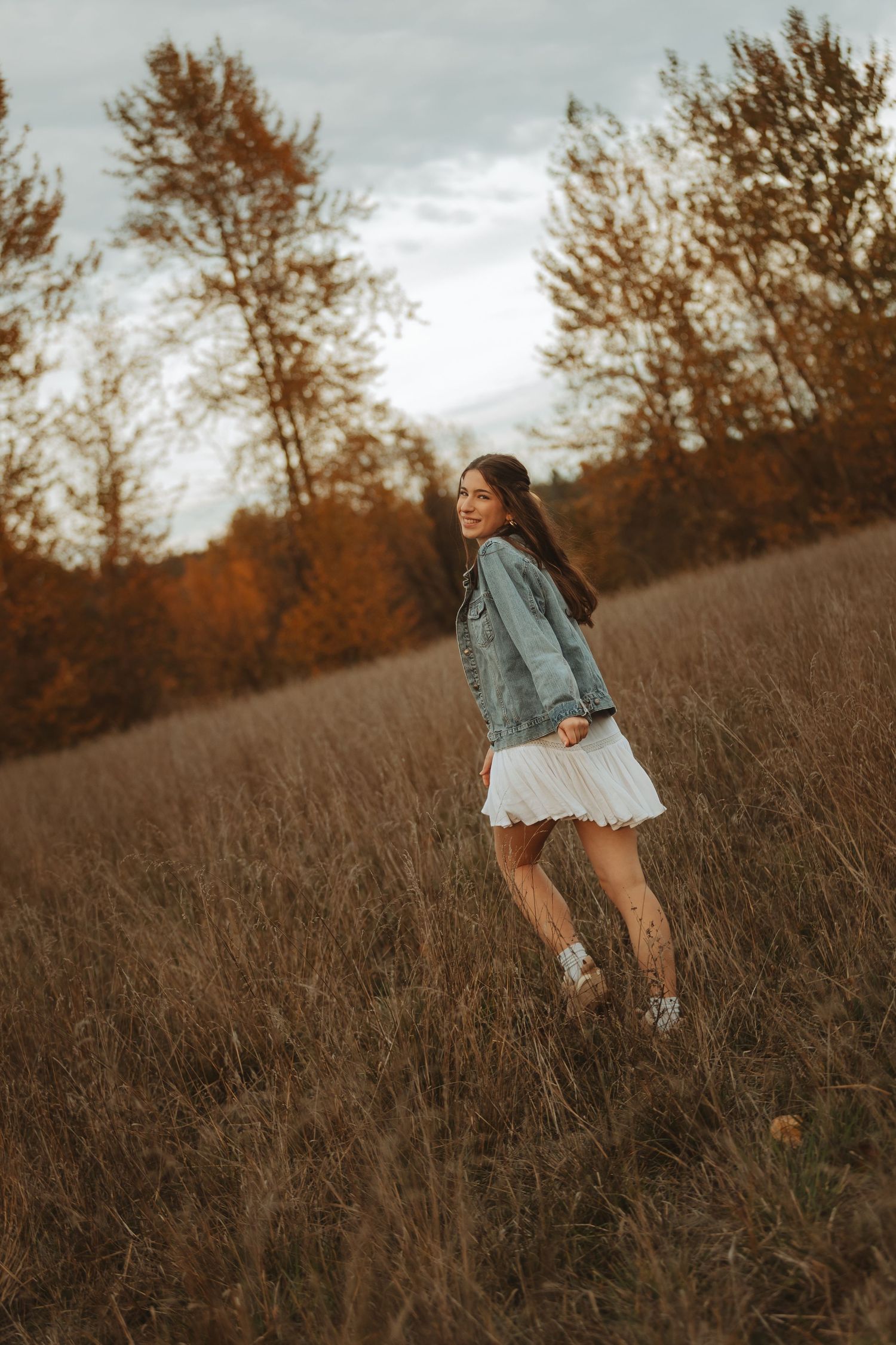 A figure in denim and white spins joyfully in a rustic field during sunset.