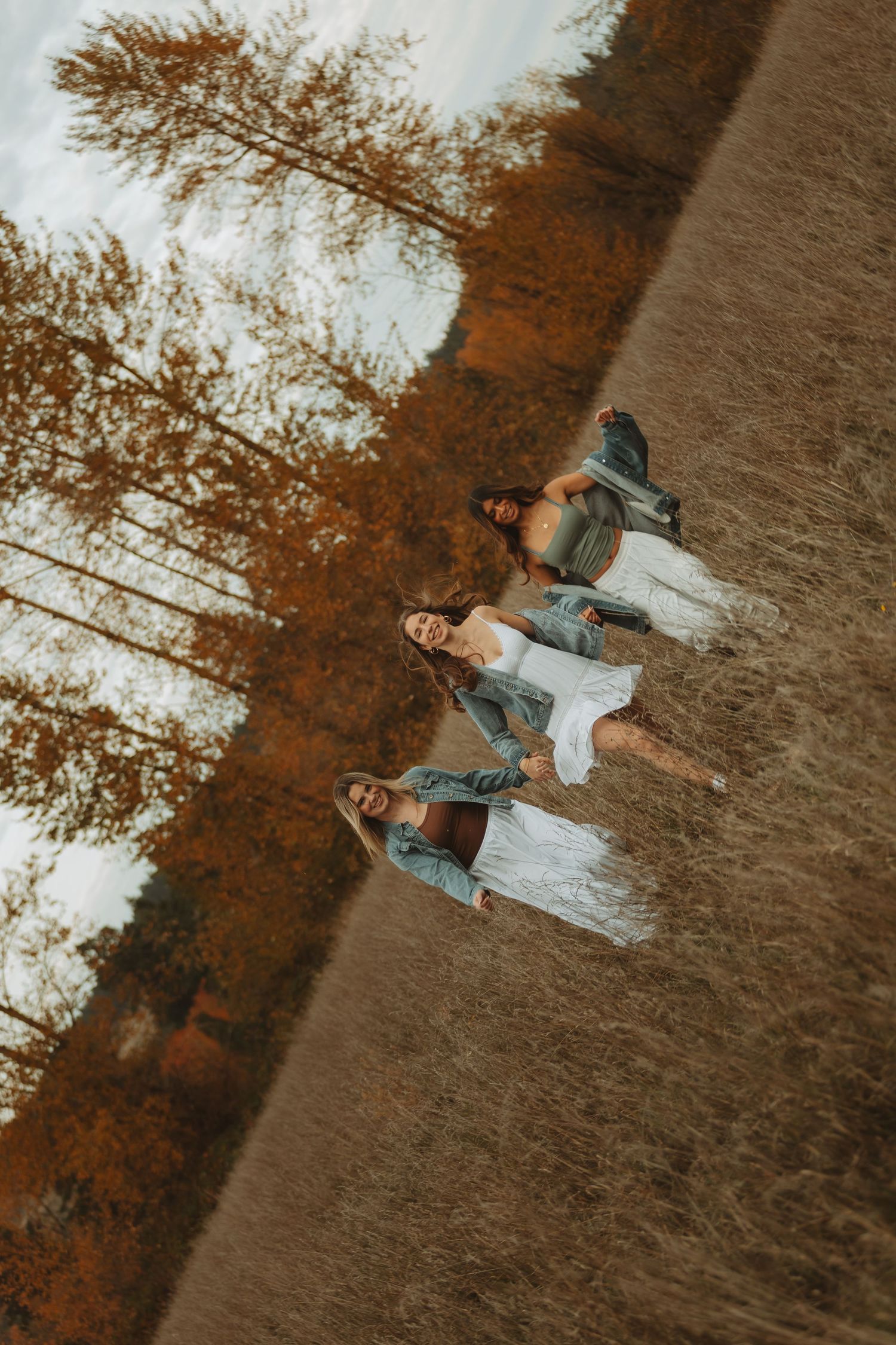 A person in denim lies in a golden autumn field surrounded by tall trees at sunset.