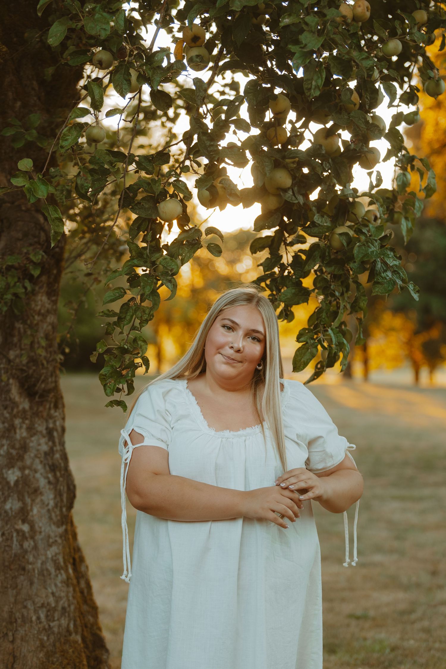 A white dress is photographed in a golden sunset under tree branches creating a dreamy outdoor portrait setting.