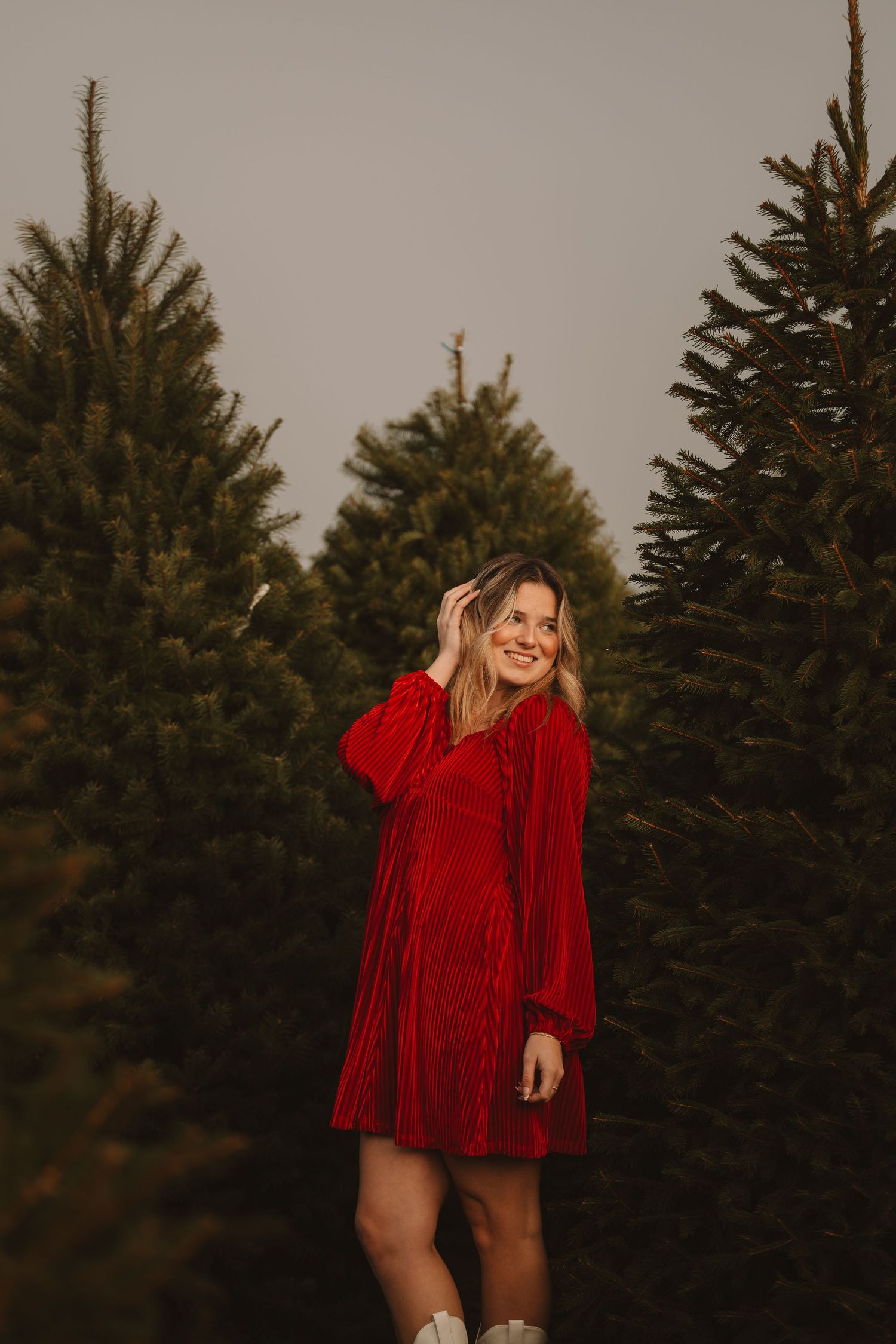 A person wearing a bright red dress twirls joyfully in front of tall pine trees.