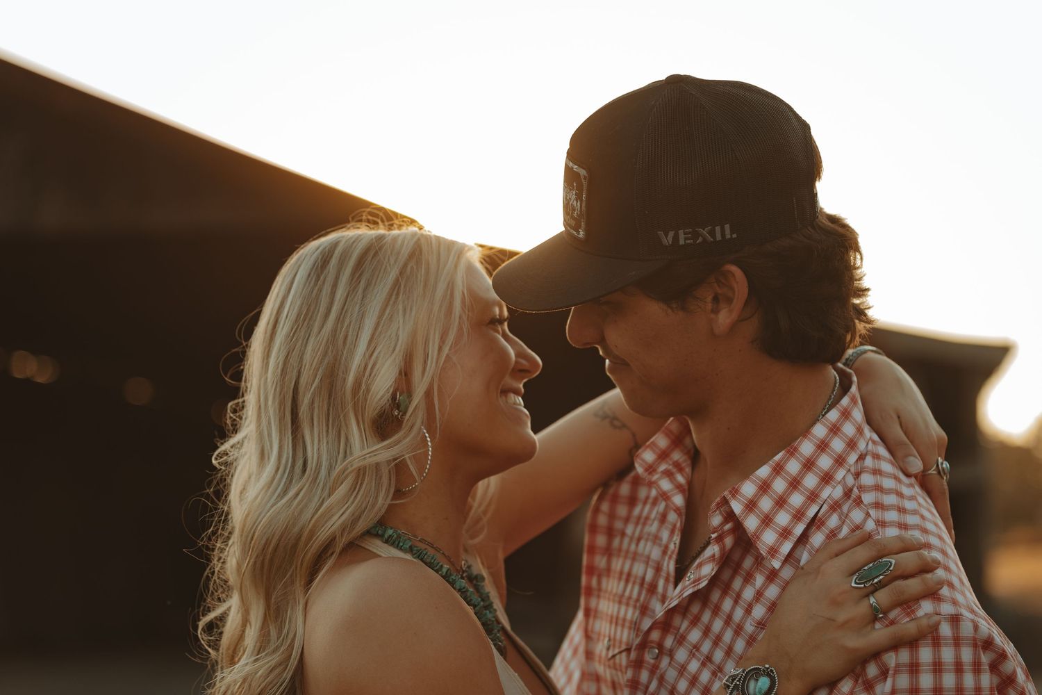 Romantic couple gazing at each other at golden hour, man wearing a trucker hat outdoors.