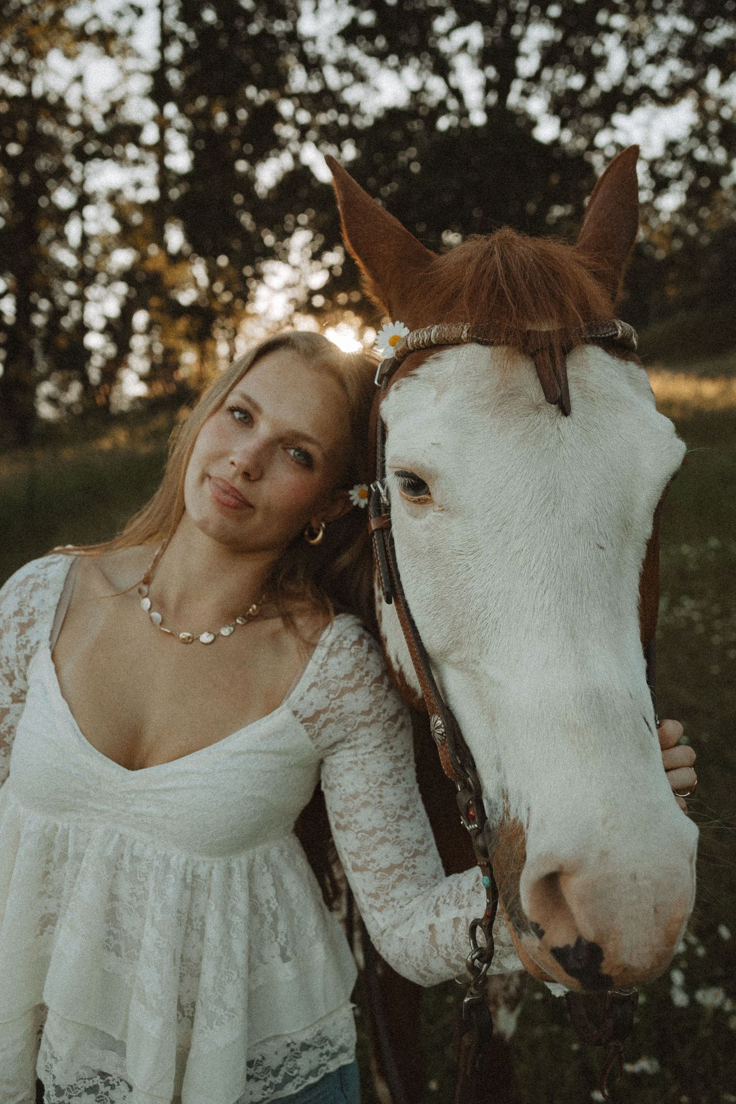 Young blonde woman in white lace dress posing cheek-to-cheek with a chestnut and white horse outdoors.