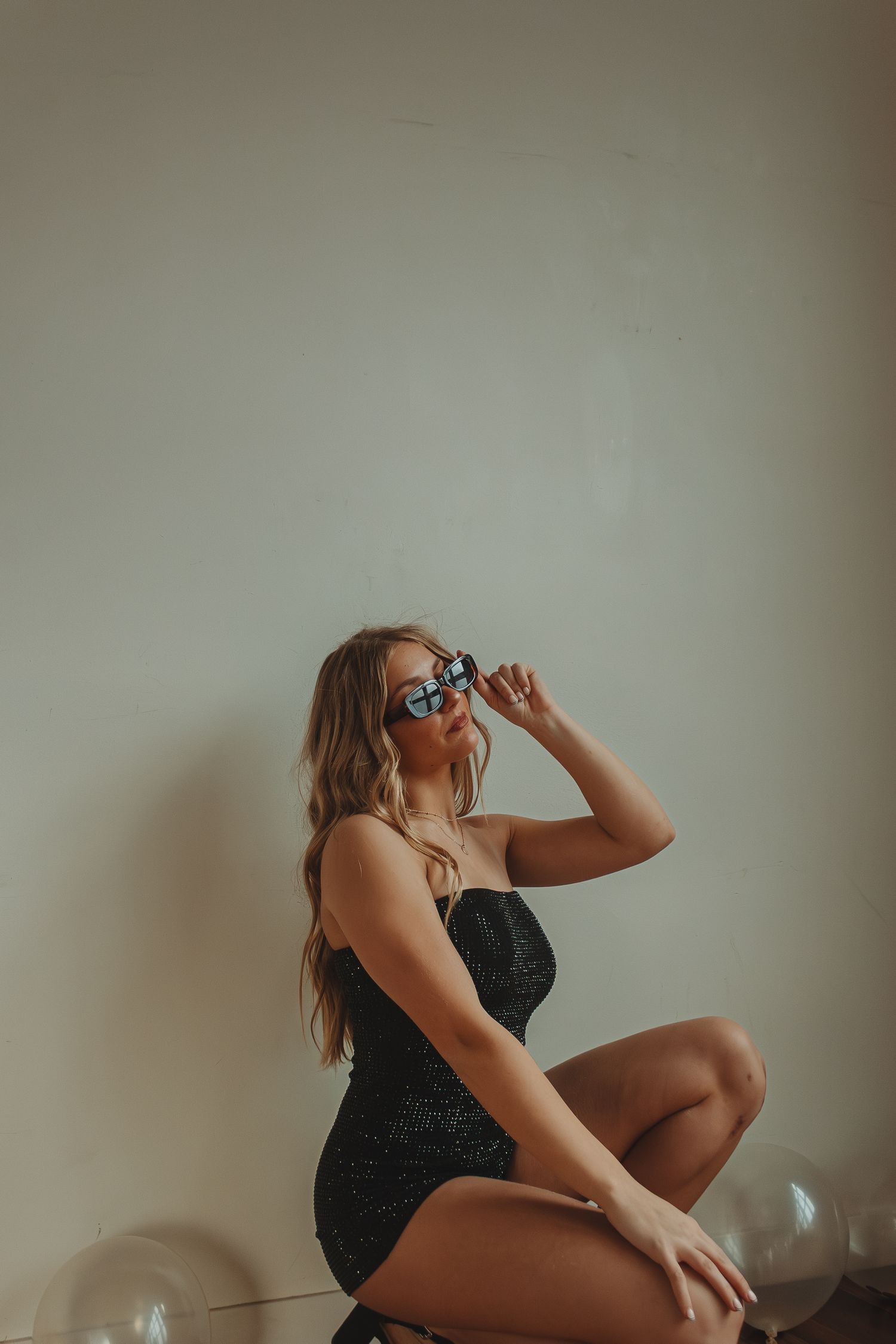 Person in black swimwear strikes artistic pose with balloons on hardwood floor.