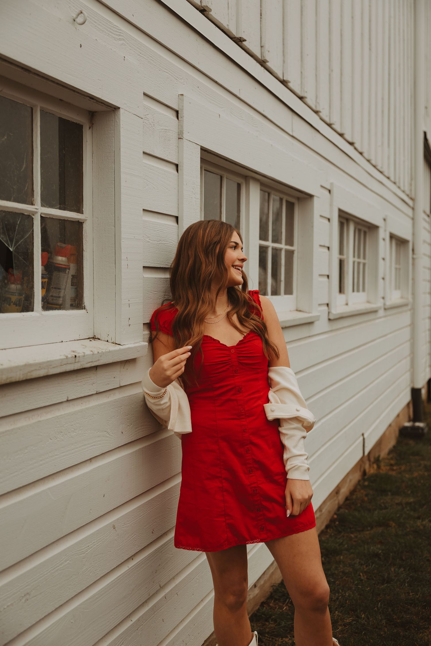 A series of photos showing someone in a red dress and cream sweater posing playfully against a white building exterior.