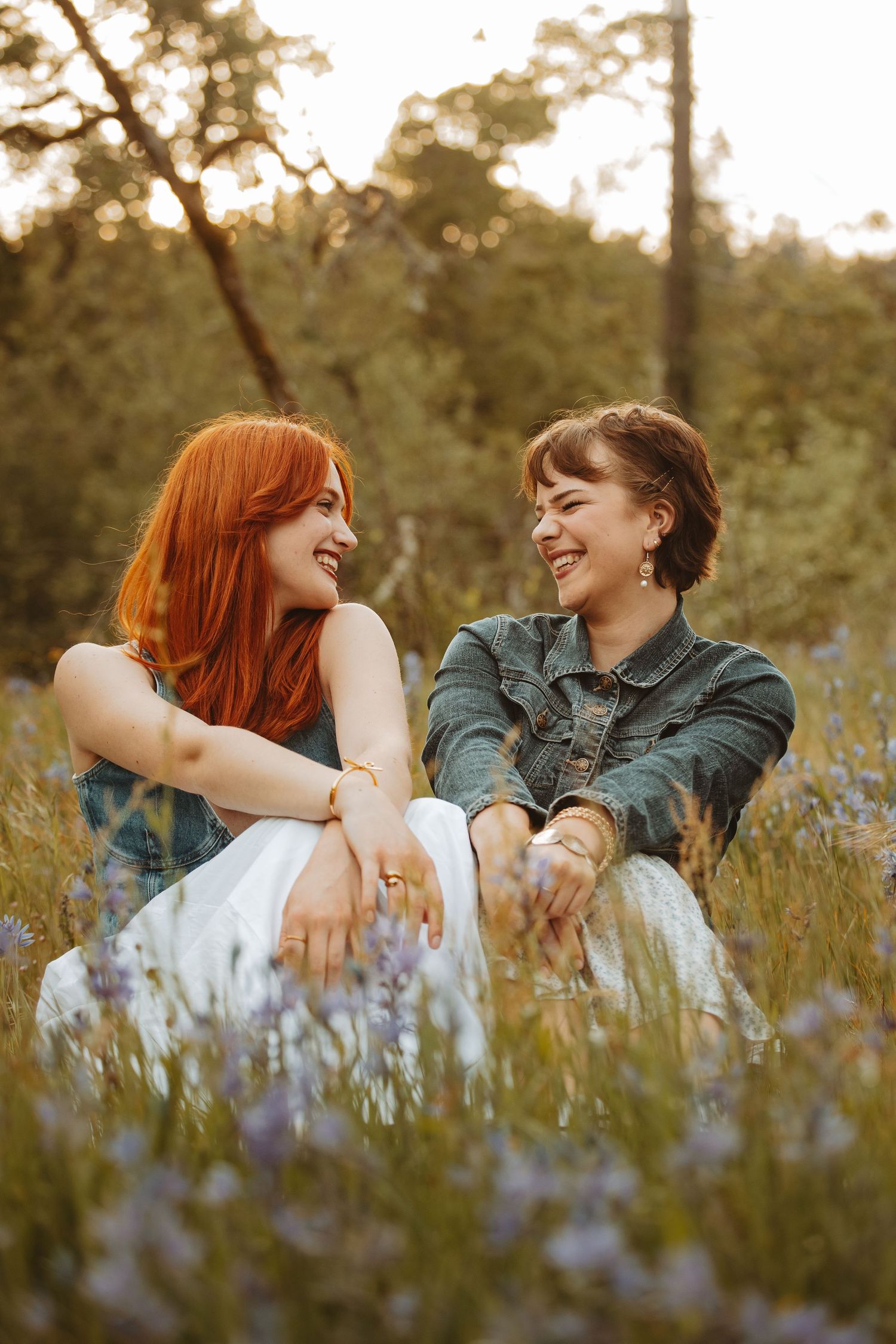 Two people sharing laughs while sitting in a field of purple wildflowers at sunset.