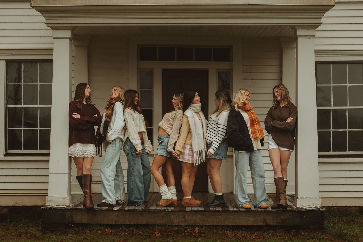 A group of people wearing casual attire stand in a line on a white porch of a traditional house.