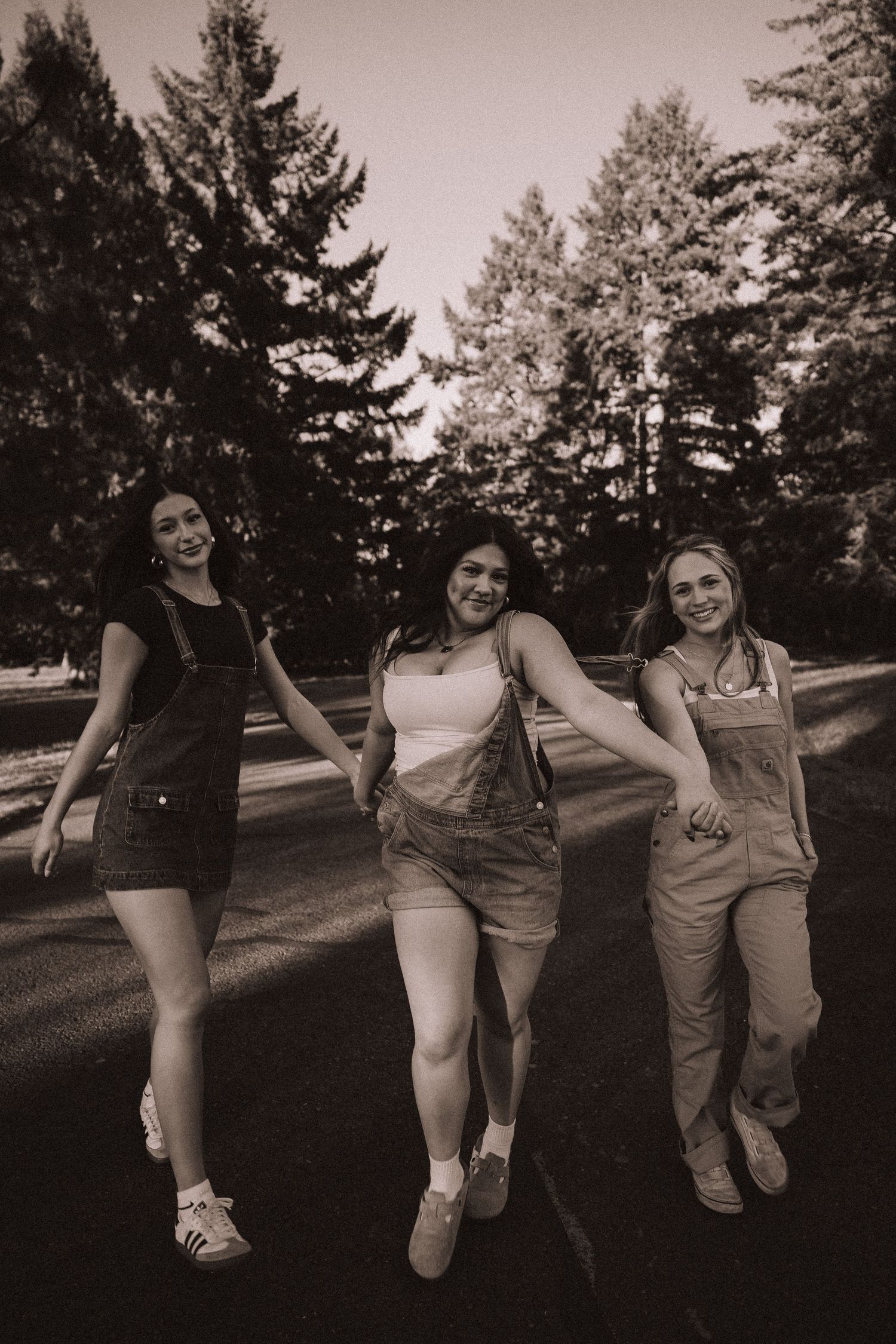 Three smiling young women in overalls walking together on a road in black and white photo.