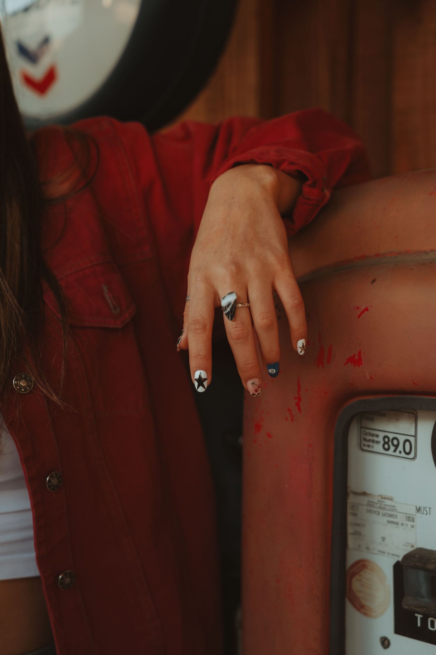 Close-up of a hand with black and white nail art resting on a vintage red gas pump.