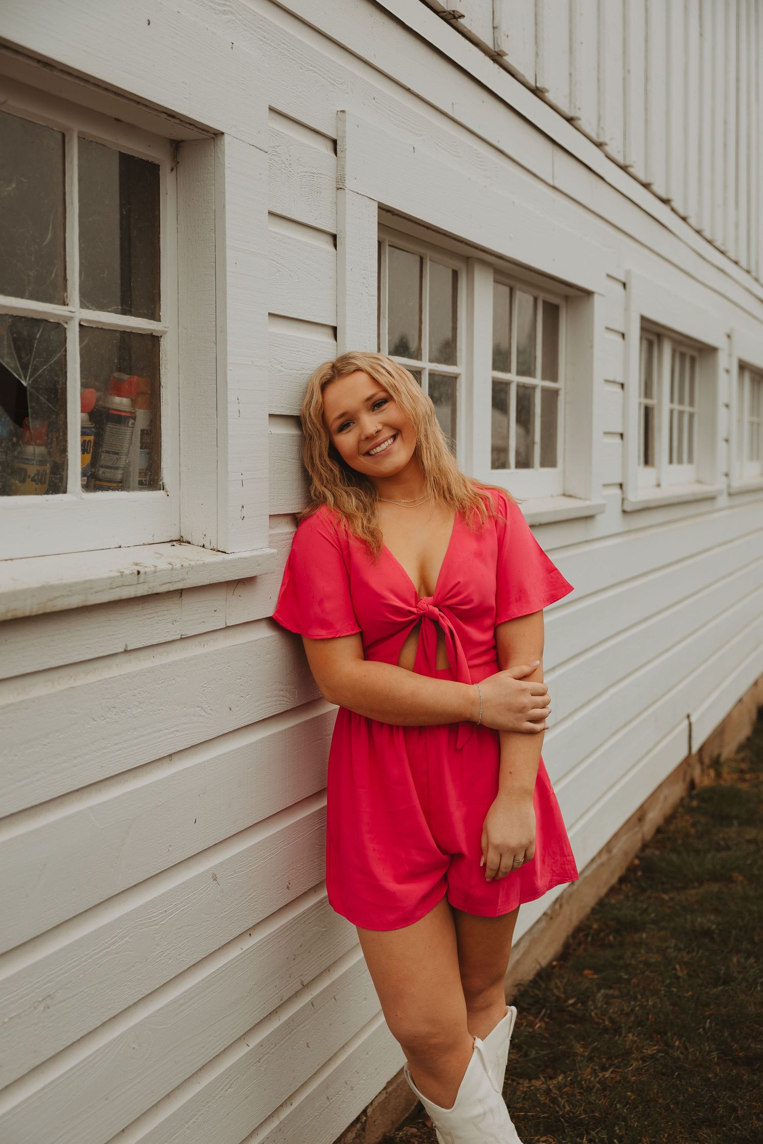 Person in bright red romper poses playfully against white building wall.