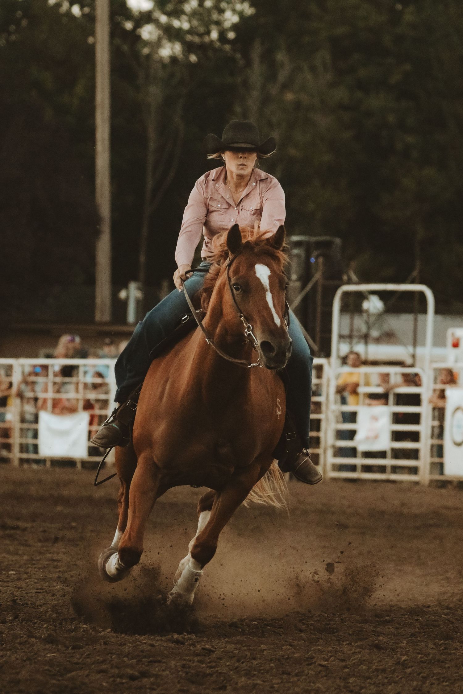 Horse and rider gallop through dirt arena during barrel racing competition.