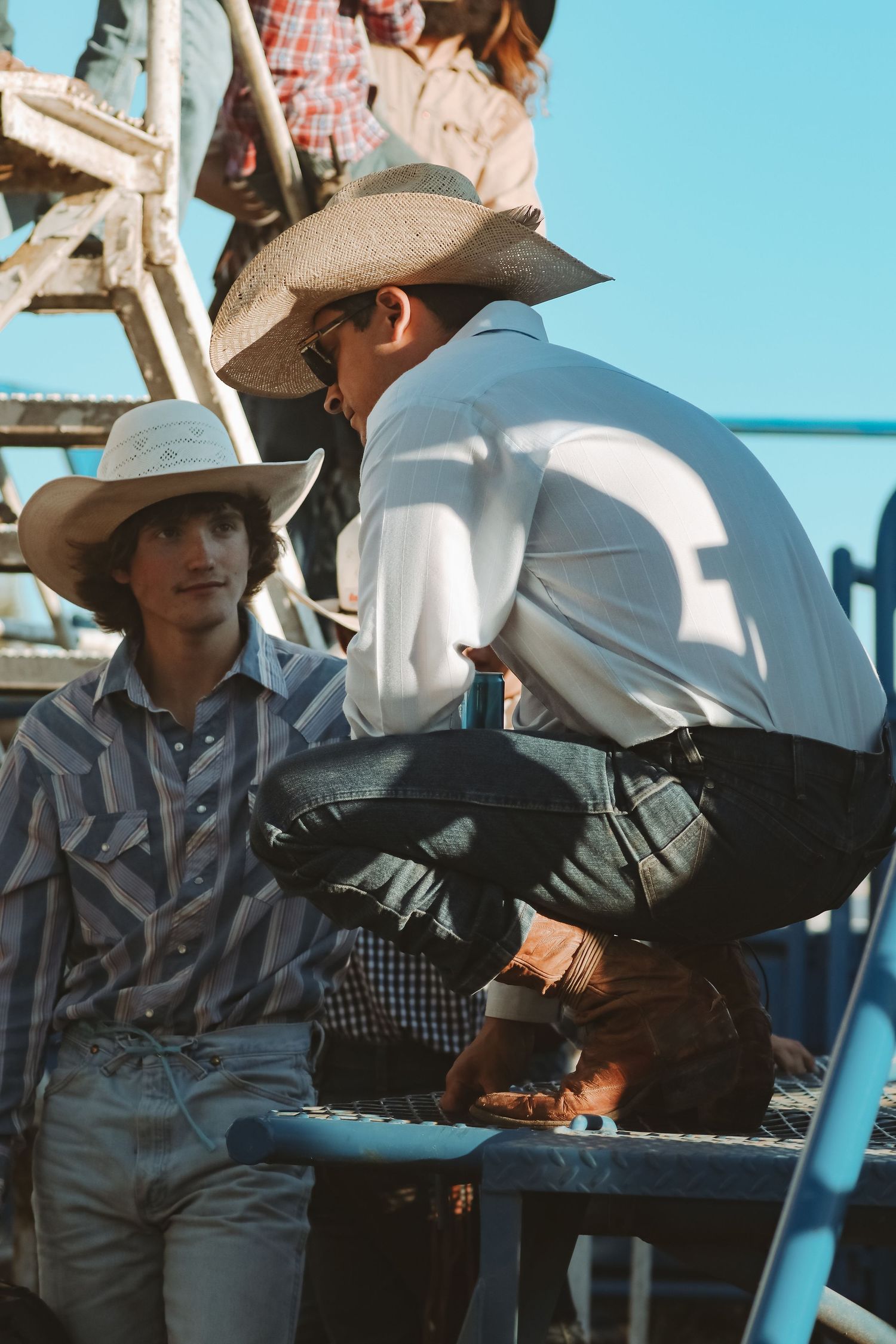 Spectators in western attire watch from bleacher seats at a rodeo event.