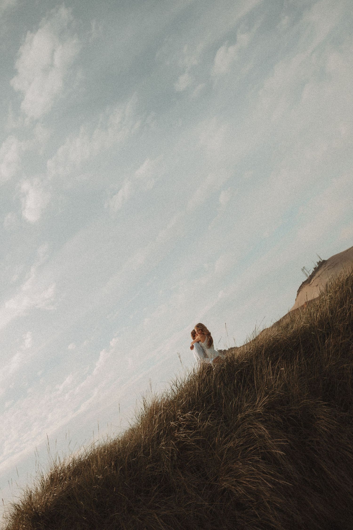 A woman in a white dress stands on a grassy hillside under a dramatic cloudy sky.