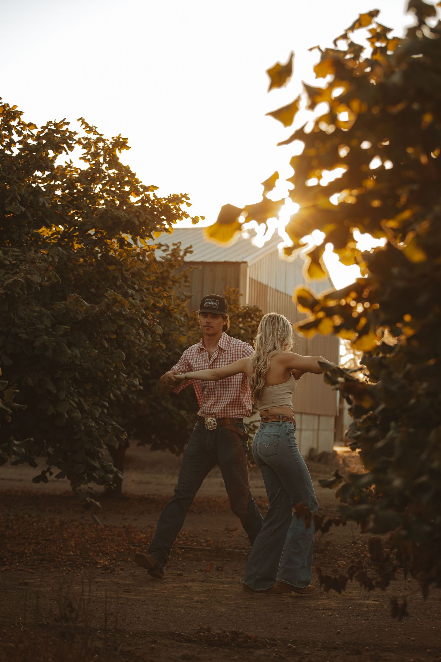 Couple dancing together at golden hour in a rustic orchard with warm sunlight filtering through trees.