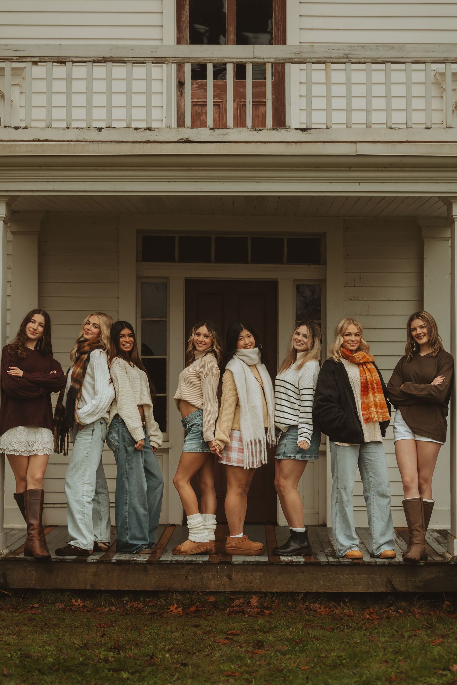 A line of people in cozy fall clothing standing on a white farmhouse porch during an outdoor gathering.