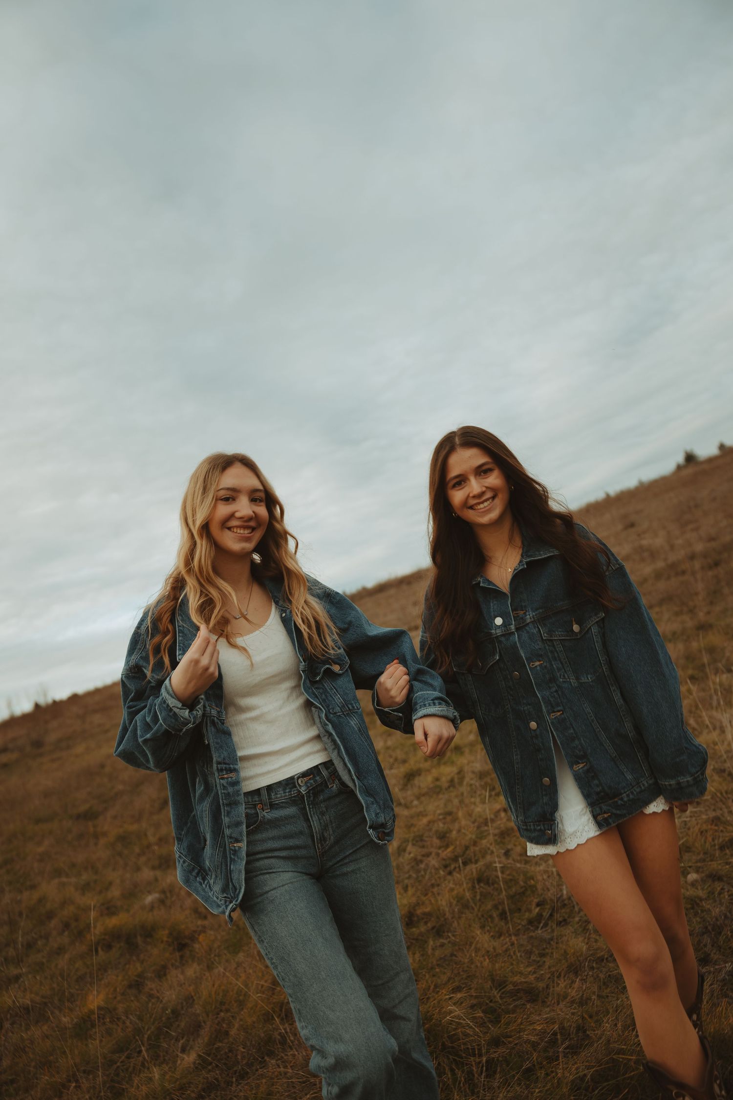 Friends in denim jackets laugh together while sitting in a golden field on an overcast day.