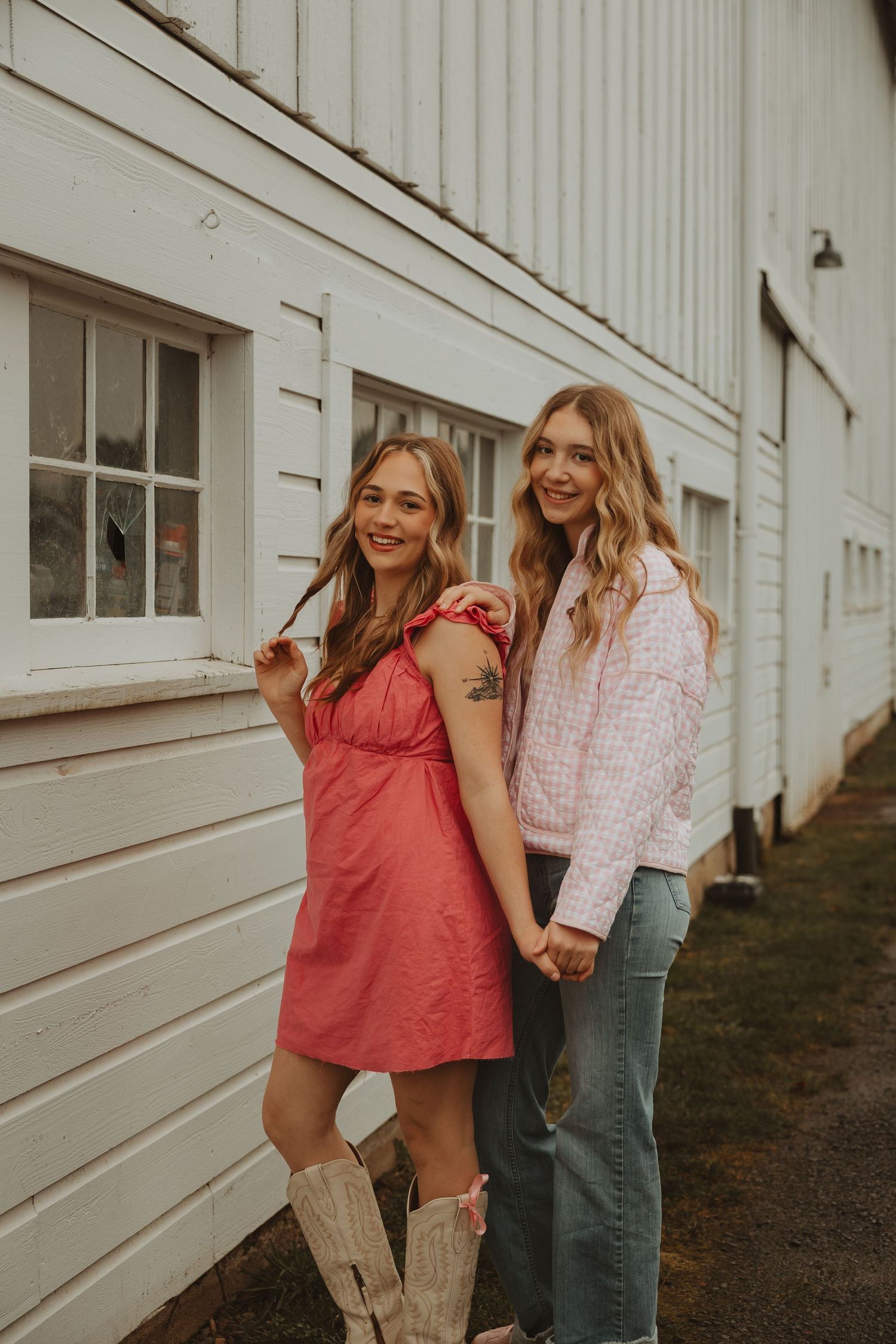 Two friends in summer outfits share candid moments against white building backdrop.