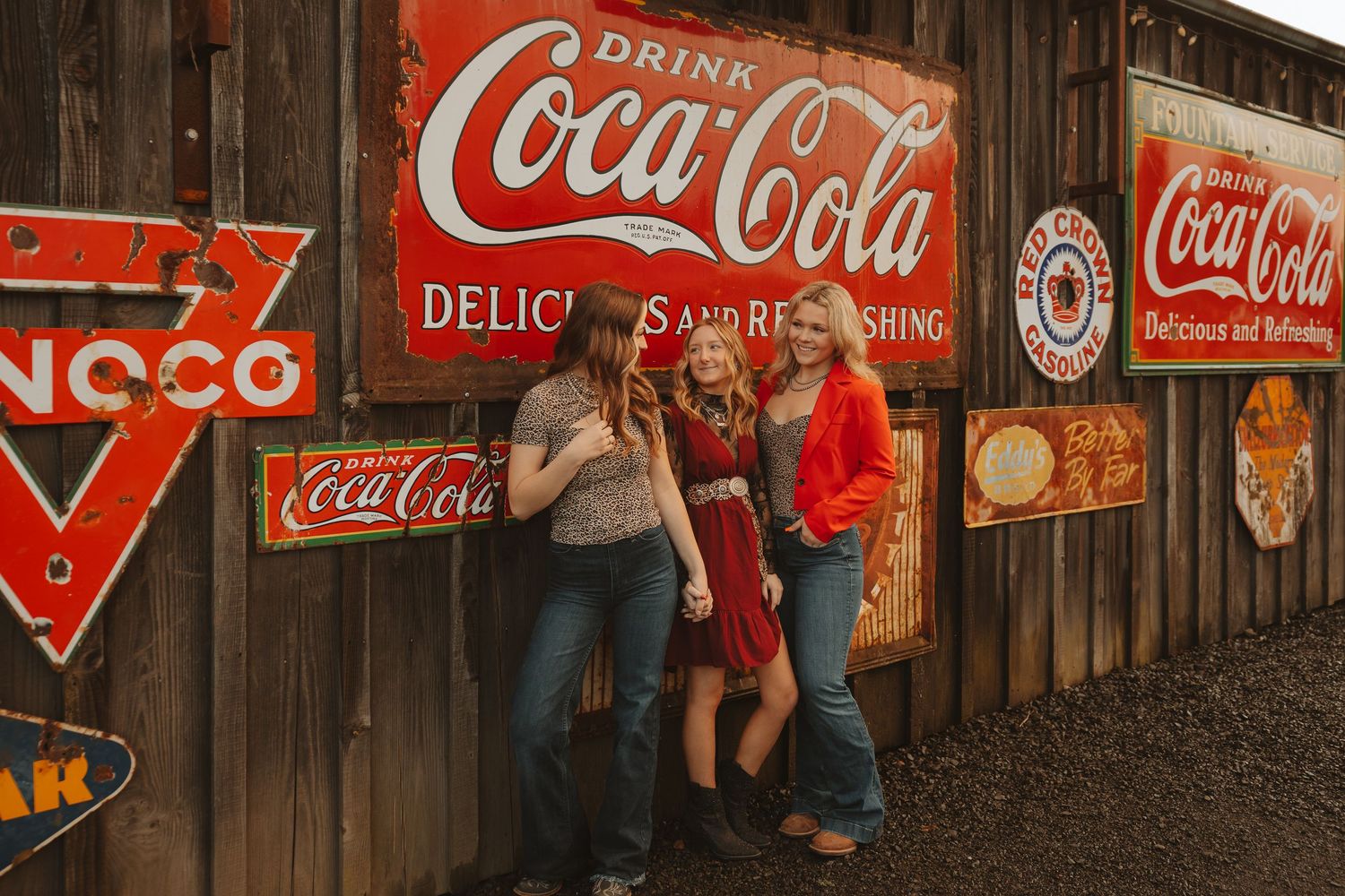 Group of friends posing and hugging near vintage Coca-Cola and NOCO signs on weathered barn wood wall.