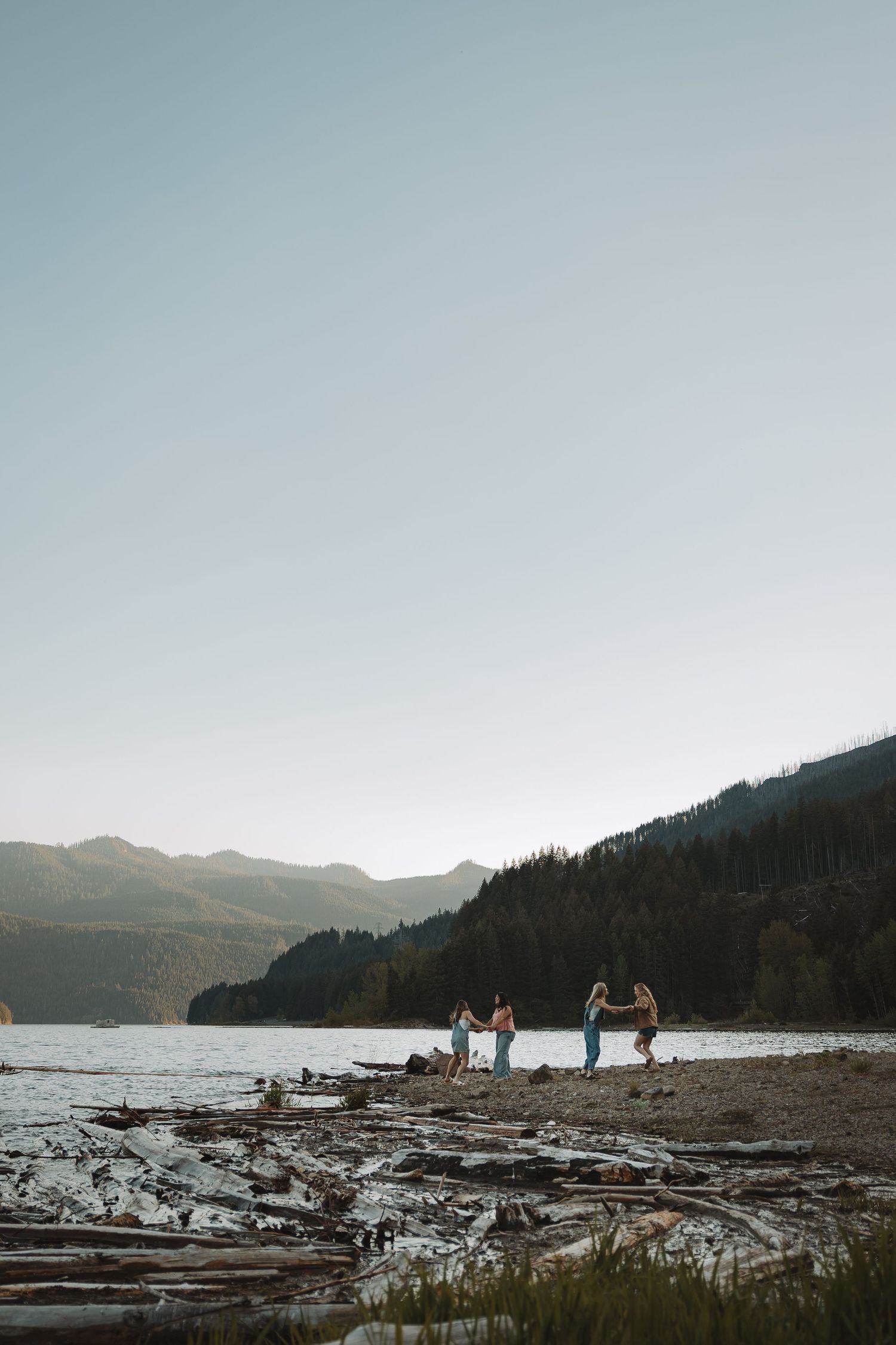 Group of friends playing on a rocky lakeshore with mountain backdrop at dusk.