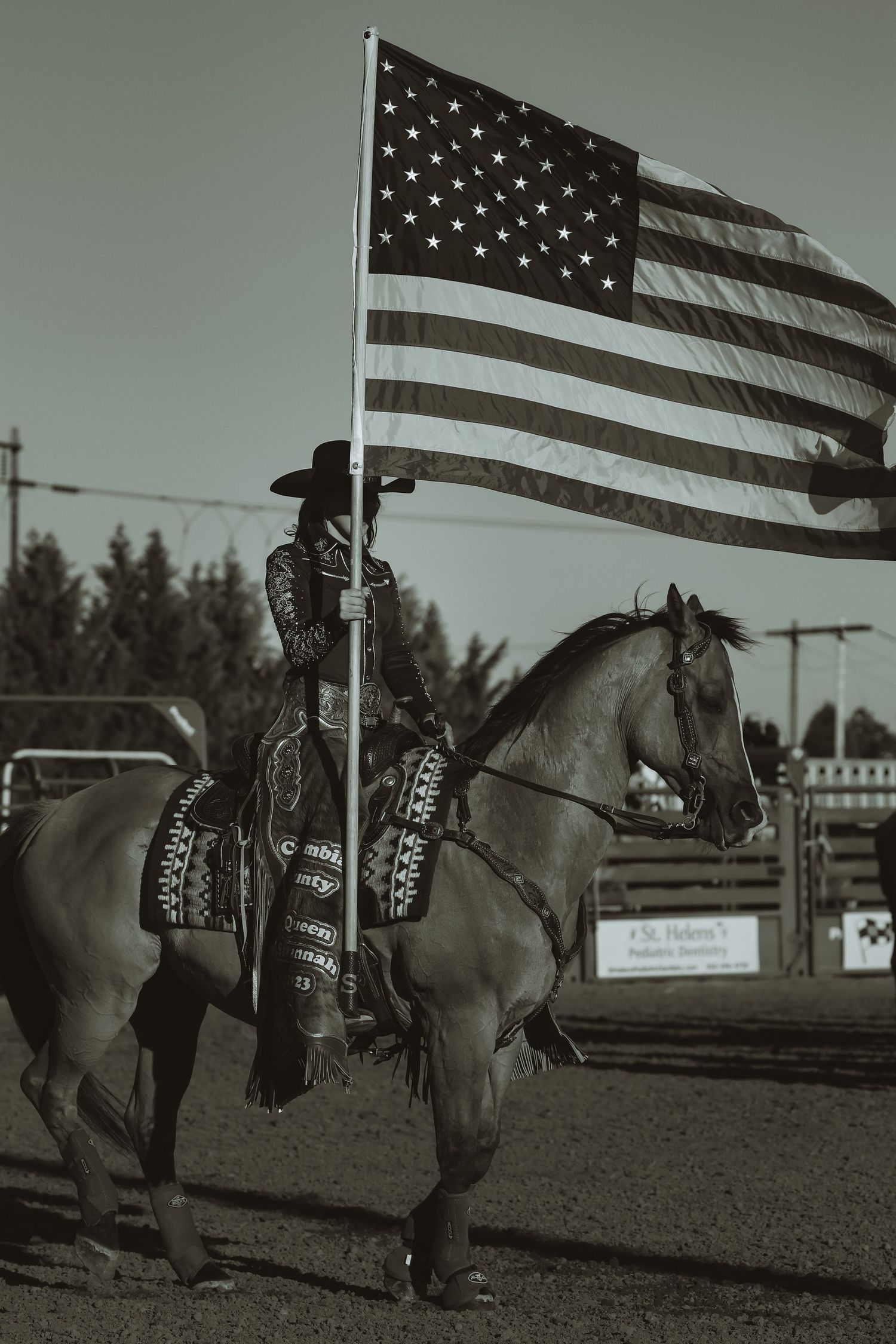 A mounted rider displays the American flag during a rodeo performance against a gray sky.