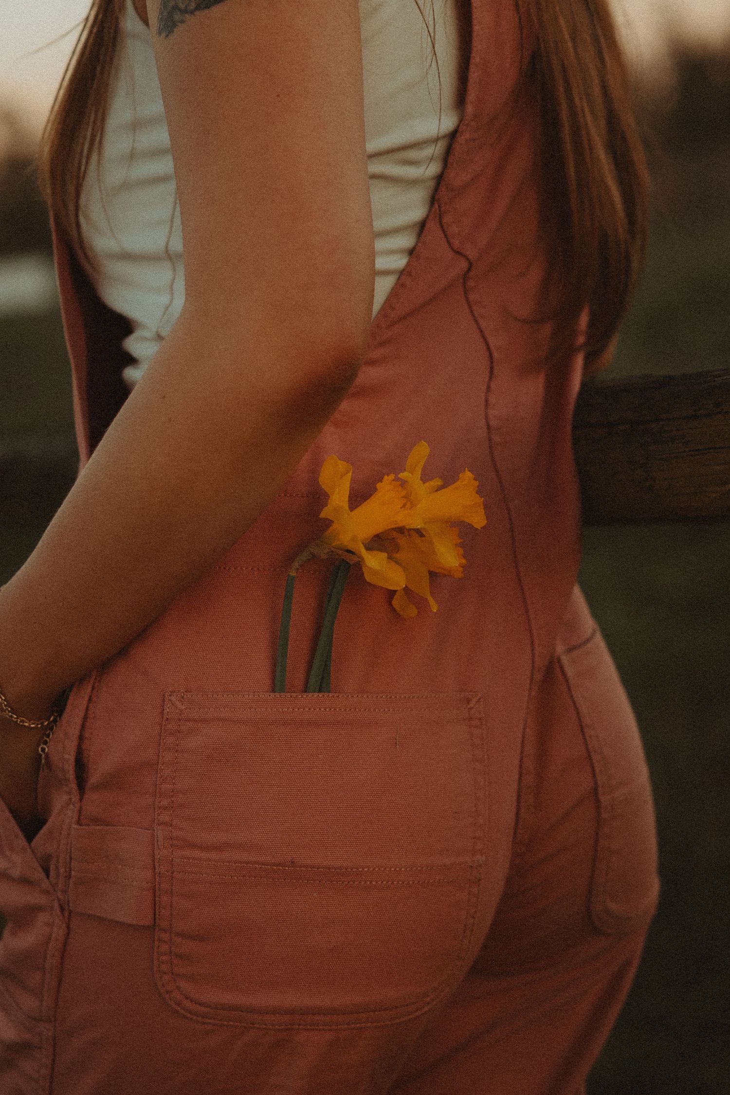 Detail shot of pink overalls pocket with yellow daffodils tucked in at sunset.