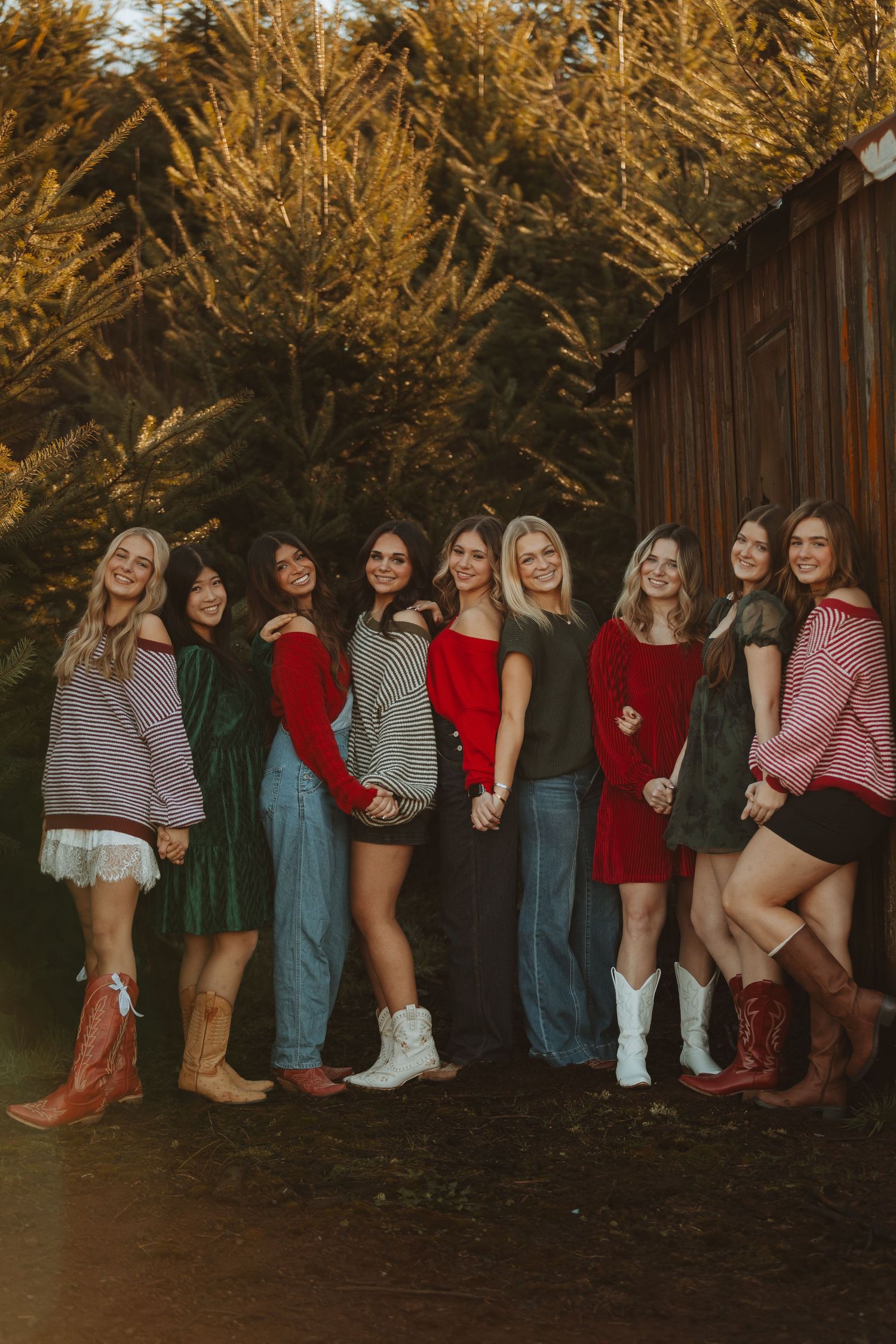 A group of friends pose together in casual fall outfits against a backdrop of golden autumn trees at sunset.