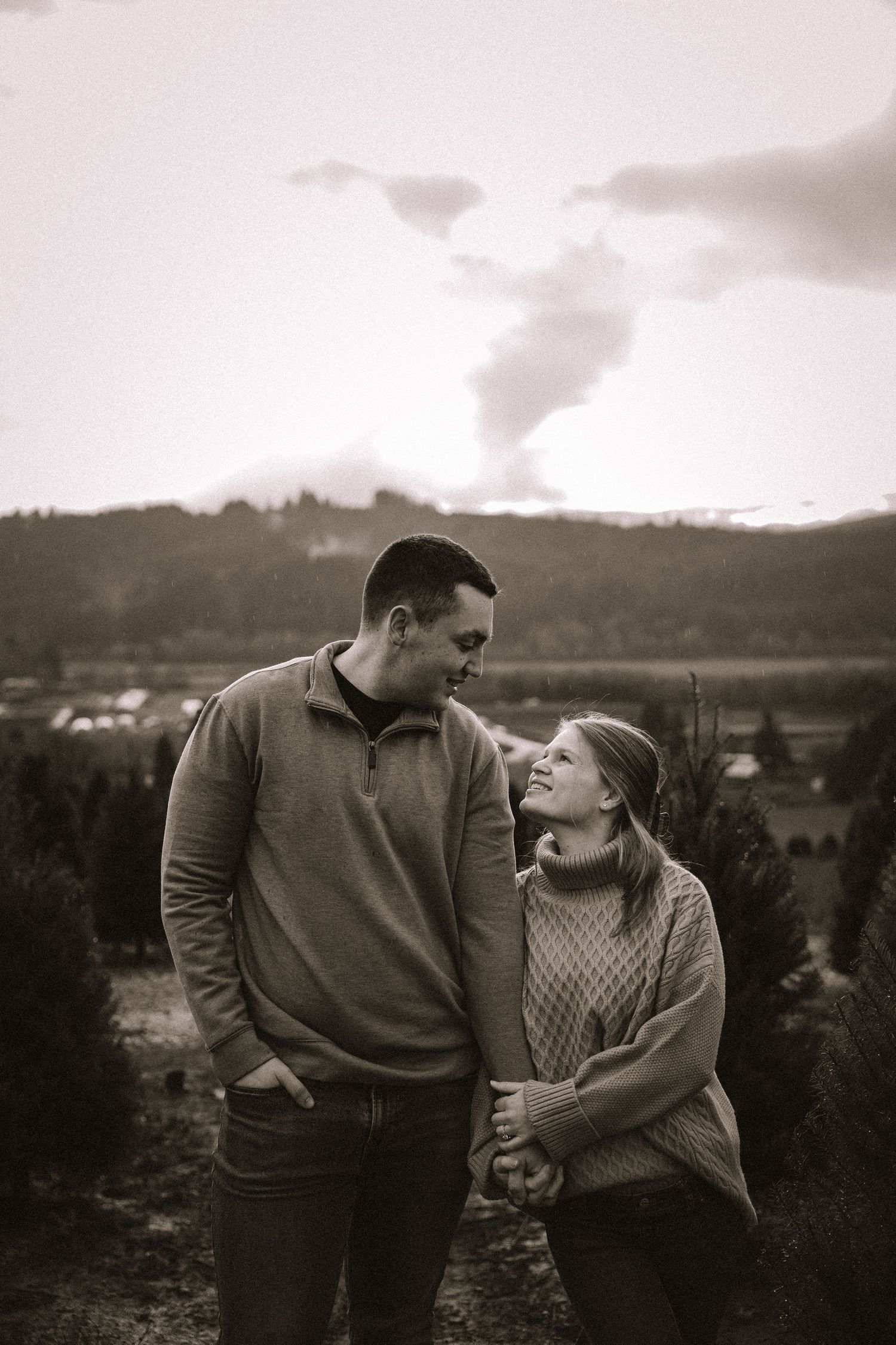 A black and white portrait of a couple sharing tender moments on a hillside overlook.