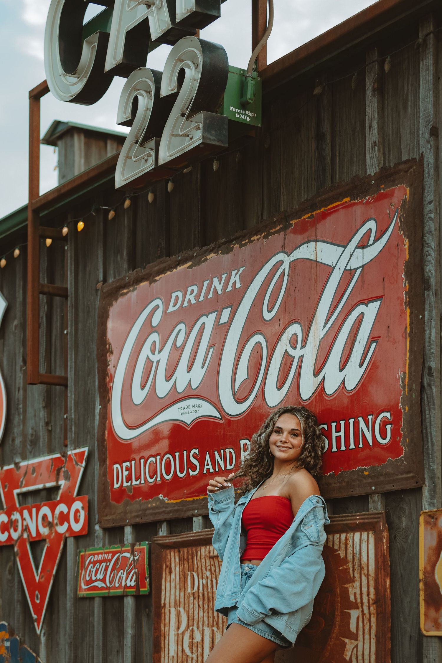 Vintage Coca-Cola sign on rustic wooden wall with string lights and retro styling.