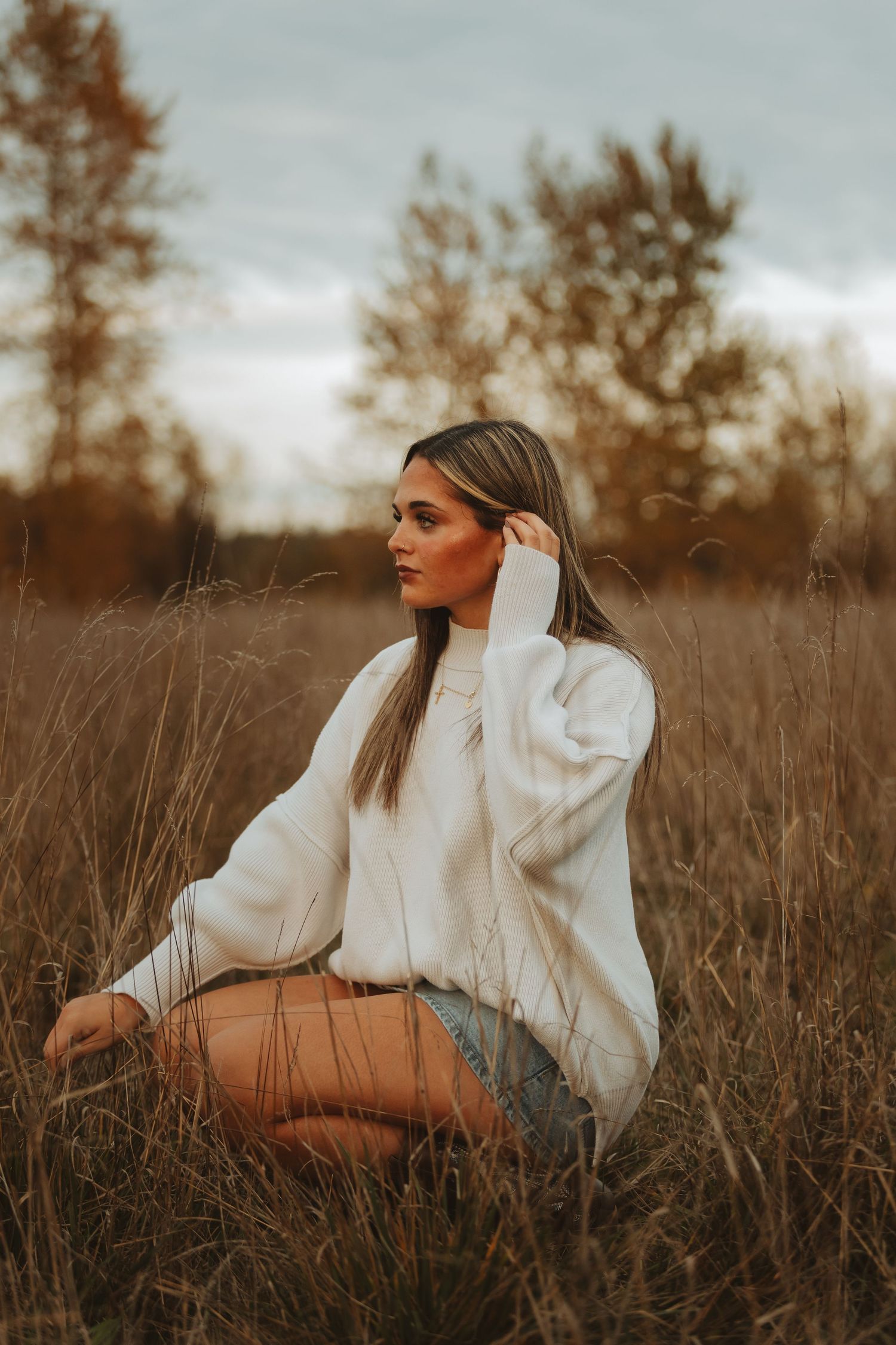 Person in white sweater poses elegantly in autumn field during golden hour.