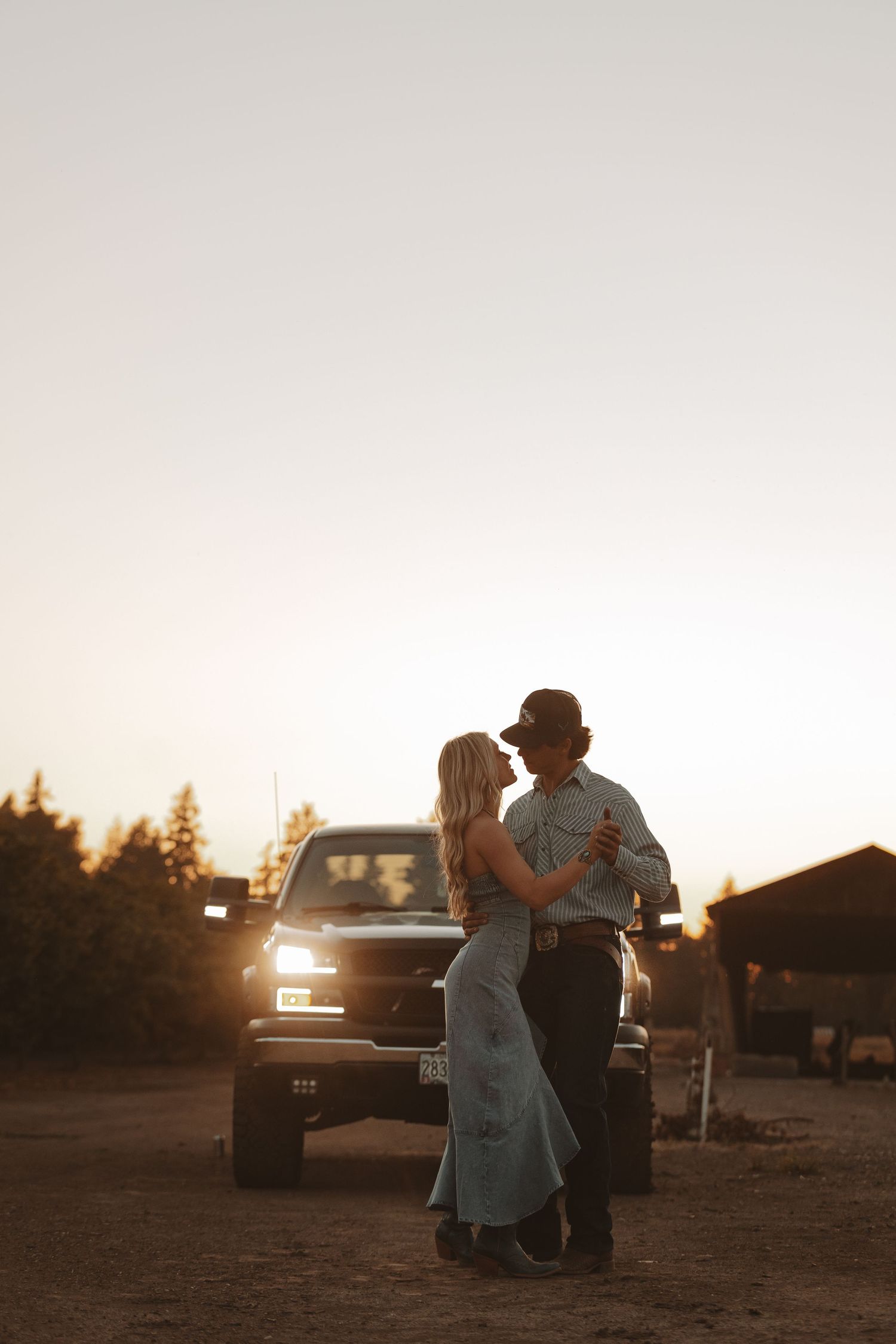 Silhouetted figures share intimate moment near parked truck at dusk.