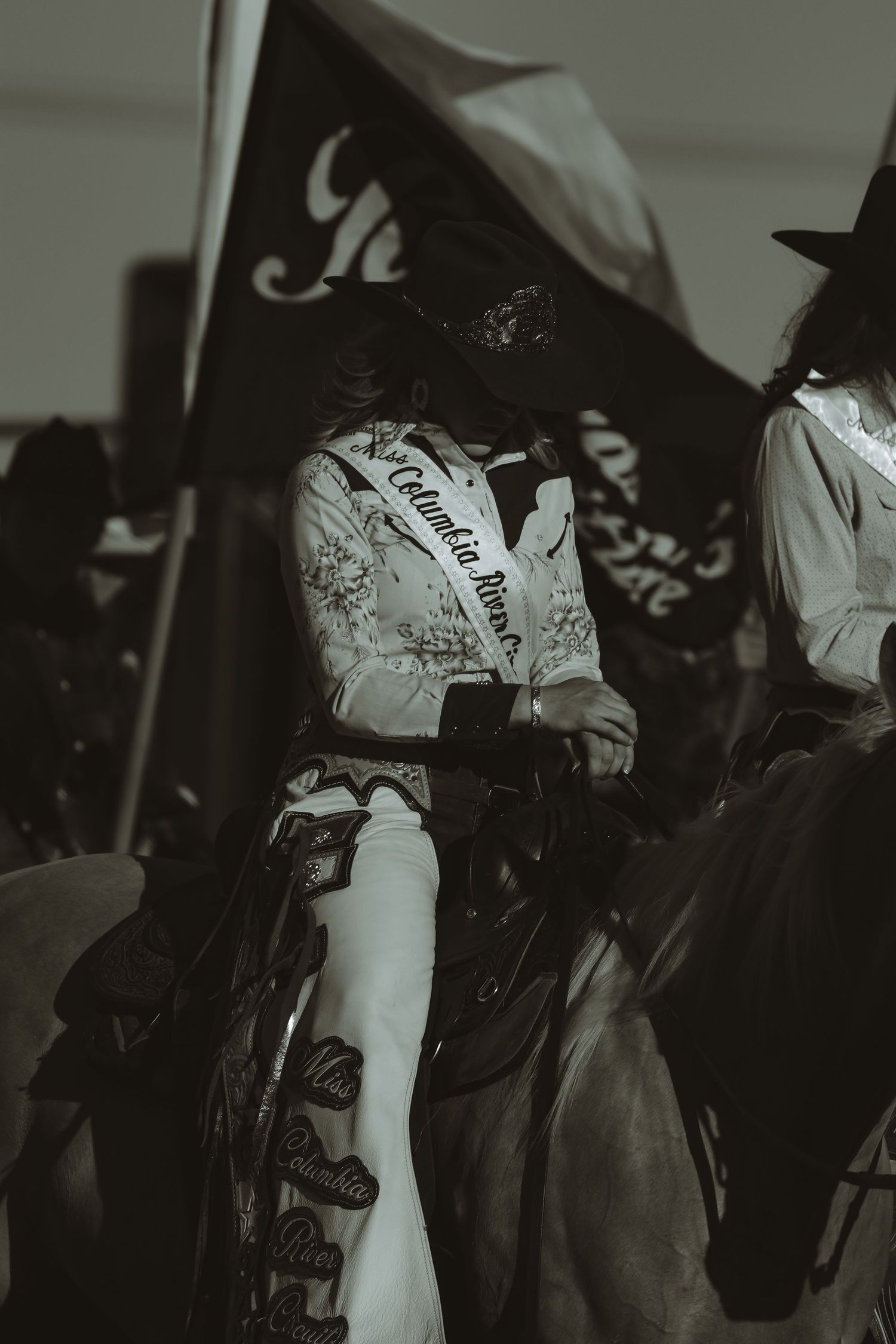 A rider in traditional western attire carries a flag while mounted on horseback at a rodeo event.