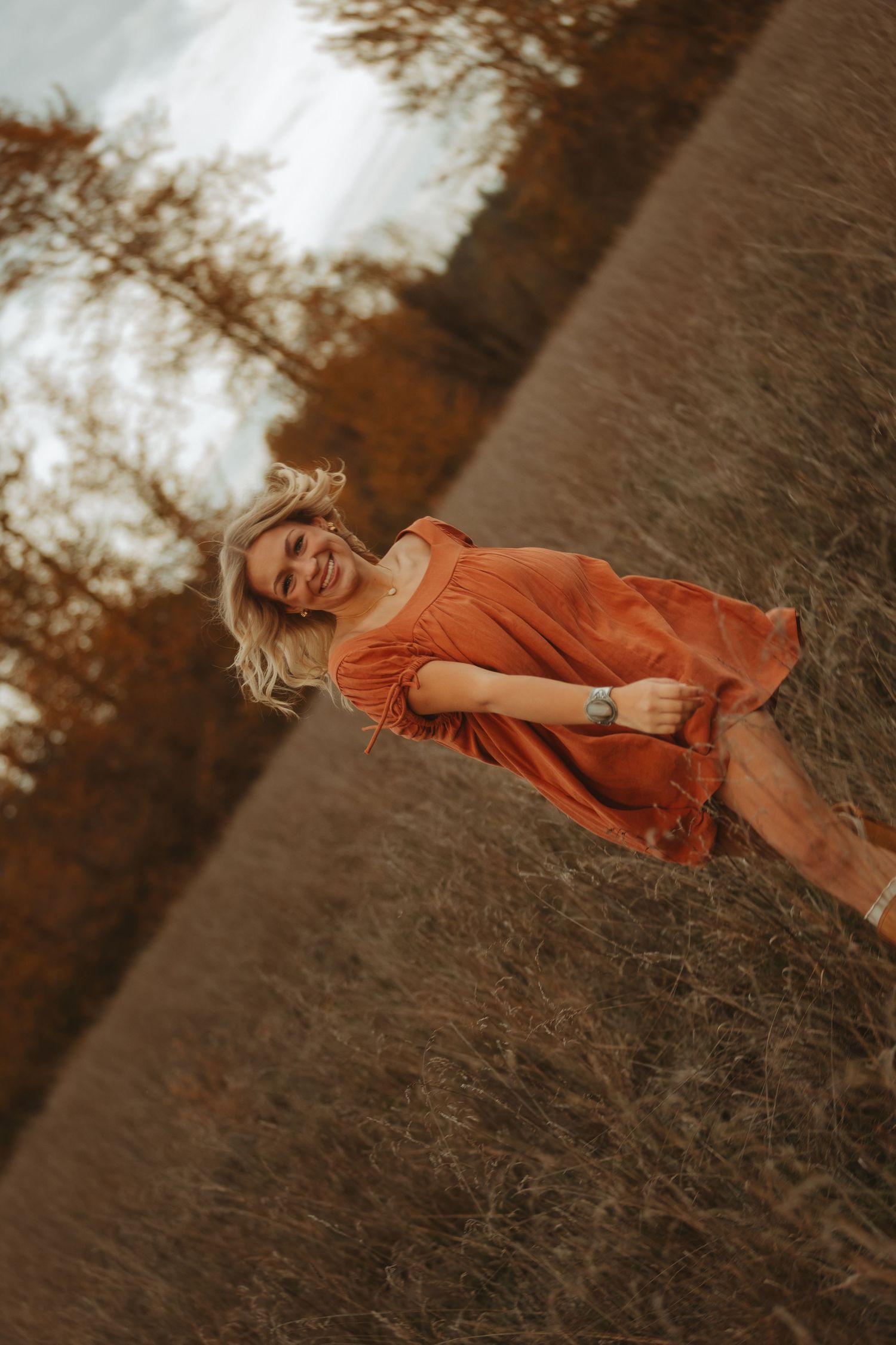 Woman in flowing orange dress poses dynamically in autumn field.