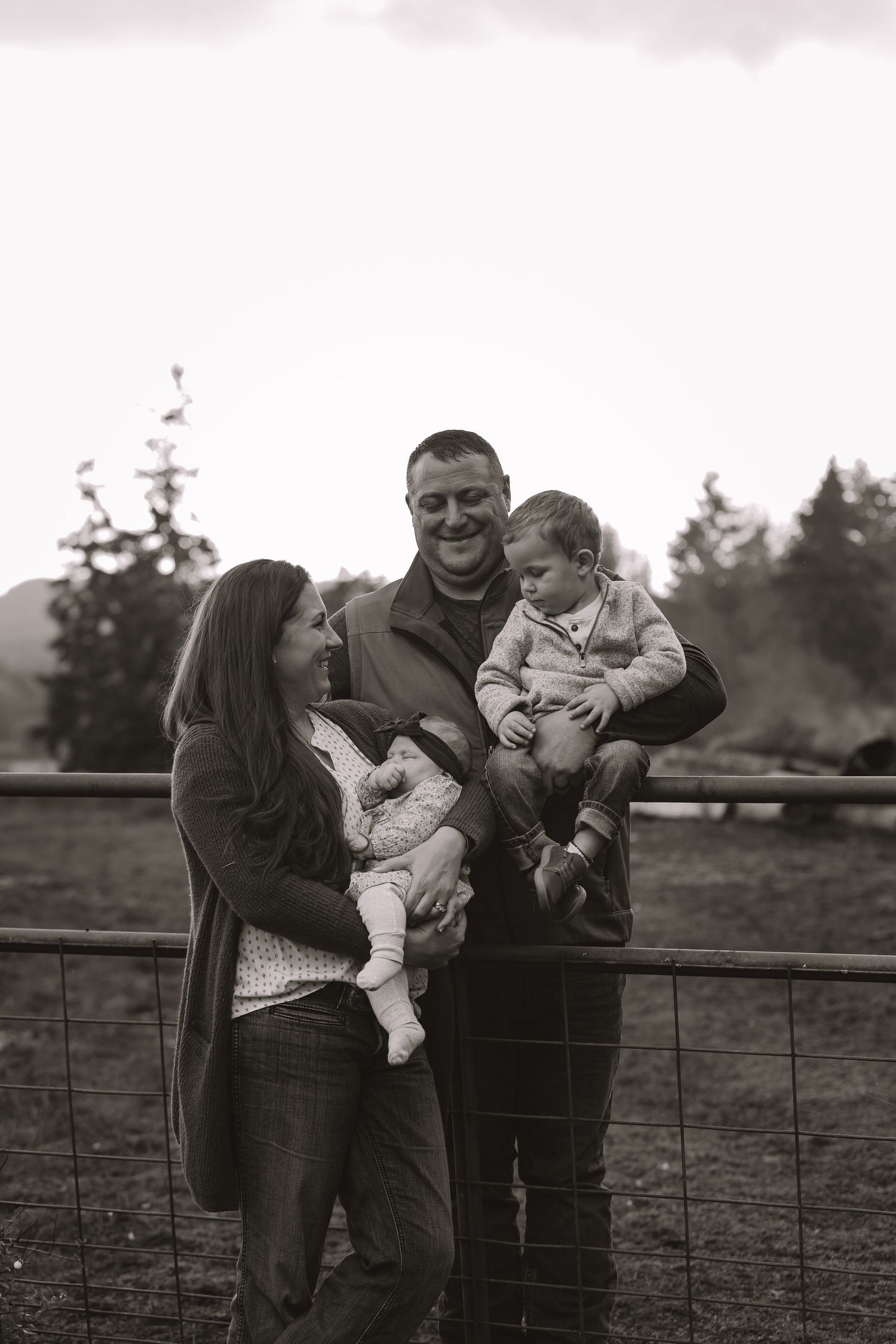 A family shares joyful moments together while standing by a rustic wooden fence at sunset.