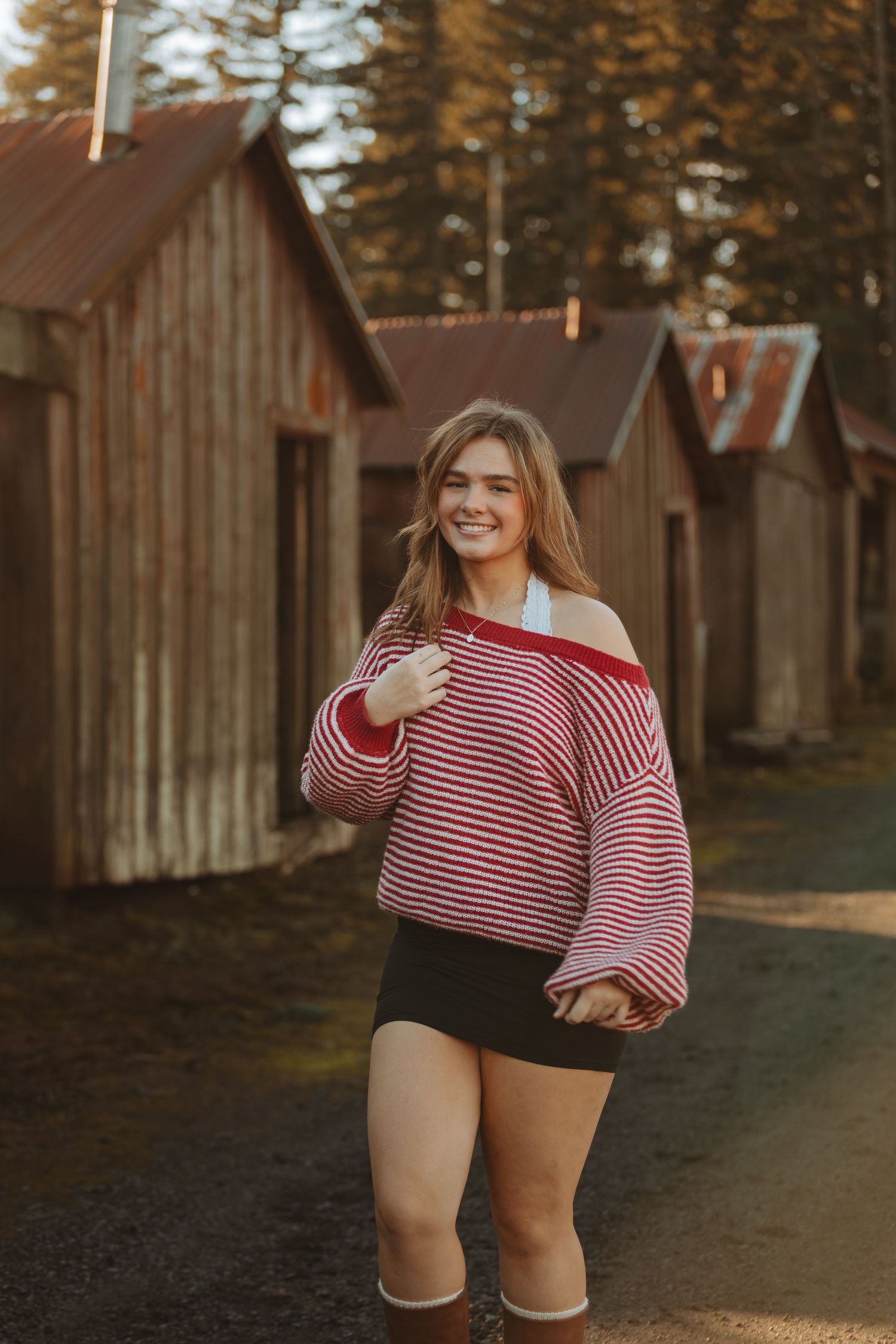 Person in striped sweater and shorts poses confidently on path between rustic cabins.