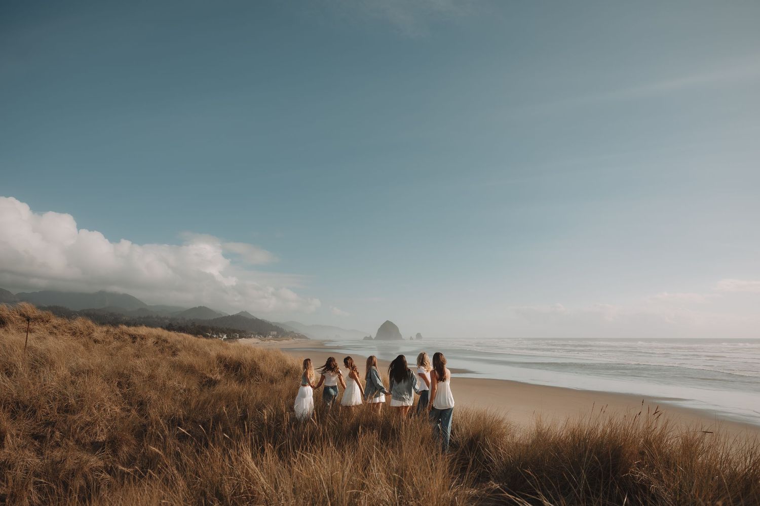 Group of women standing in coastal dune grass overlooking a scenic beach with Haystack Rock.