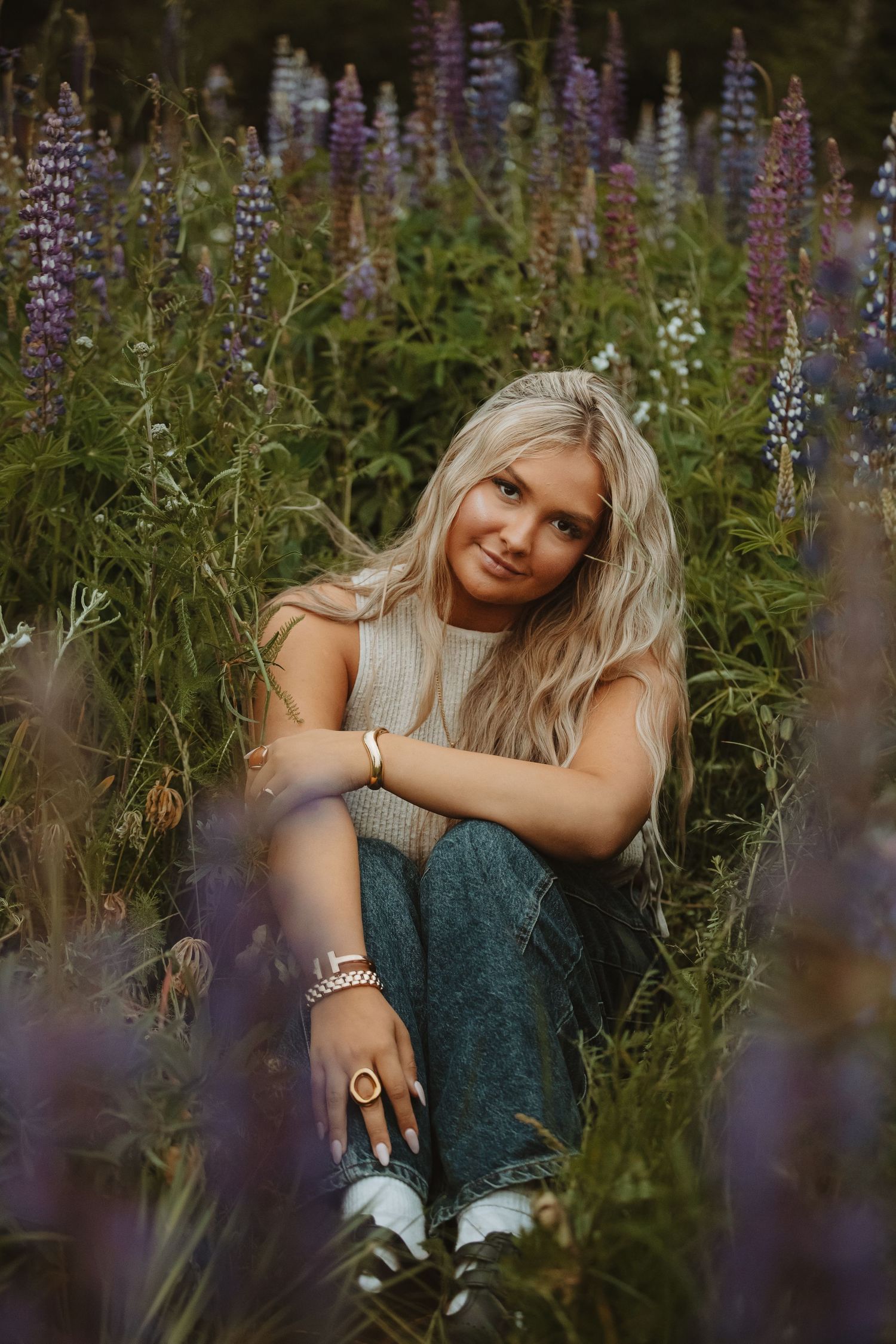 A casual portrait session features someone sitting among wild lupine flowers at sunset.