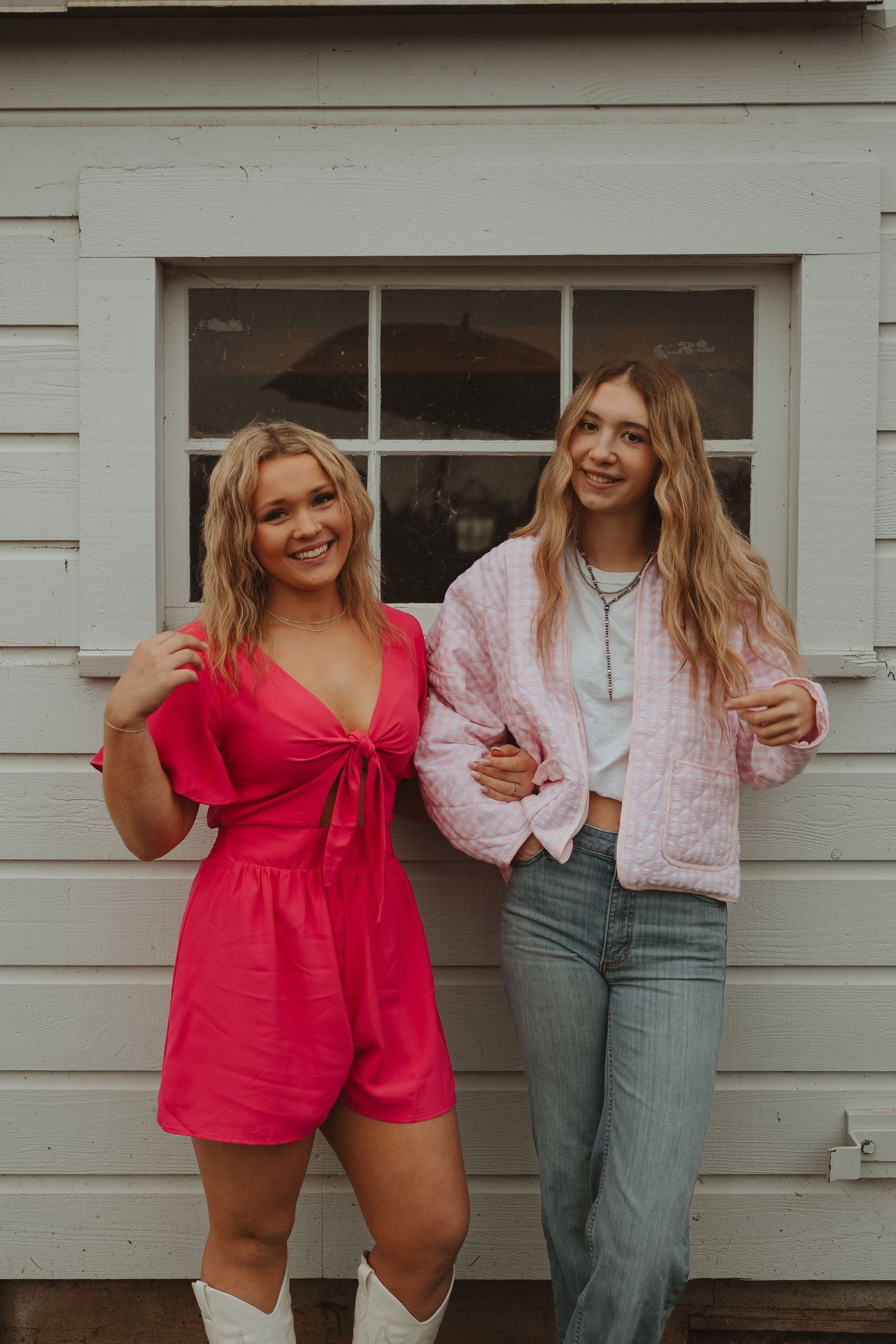 Two friends laughing together against white building wall, one wearing red and one in casual denim.