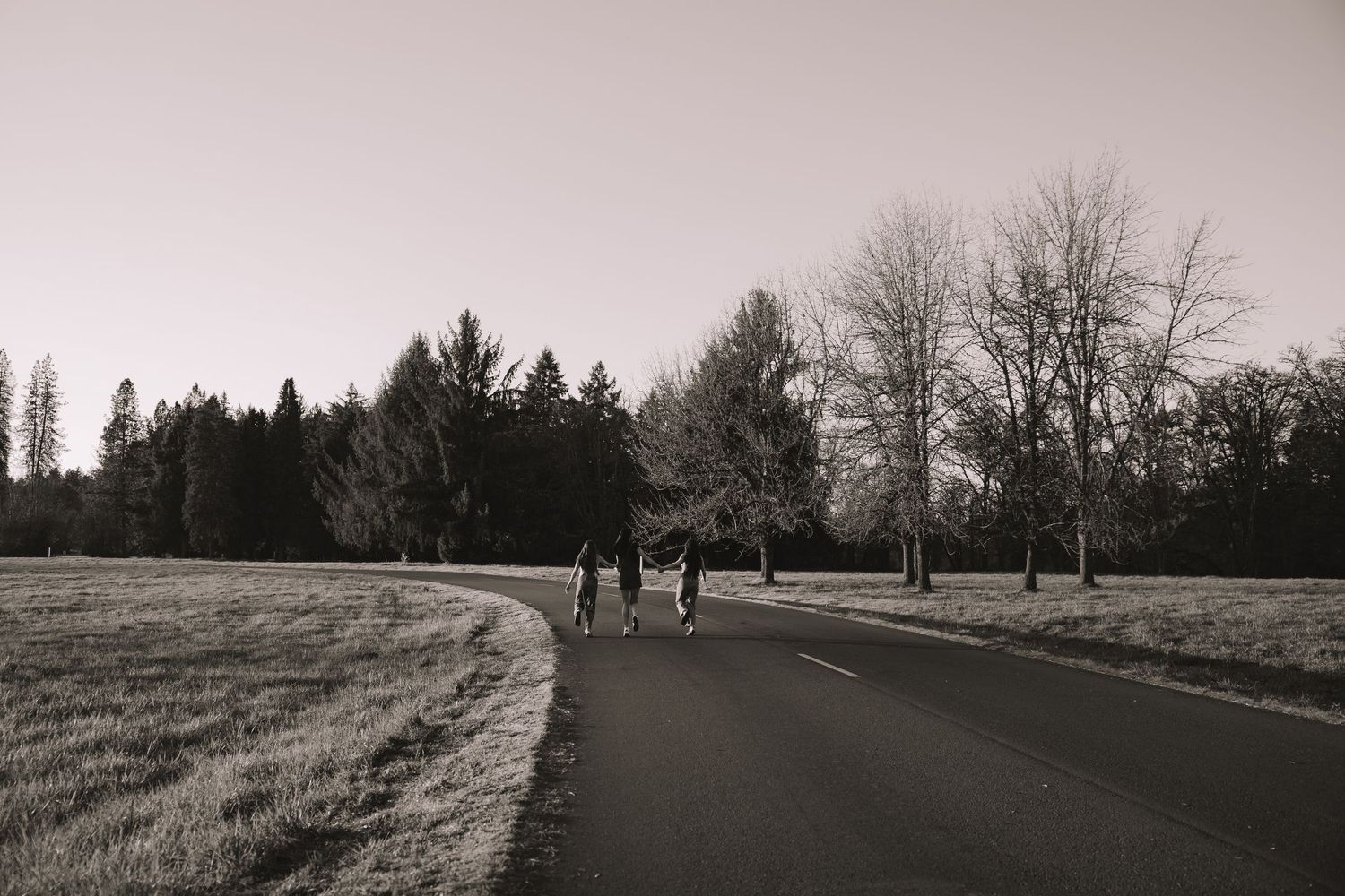 Three people walking along a curved road through an open field in black and white.