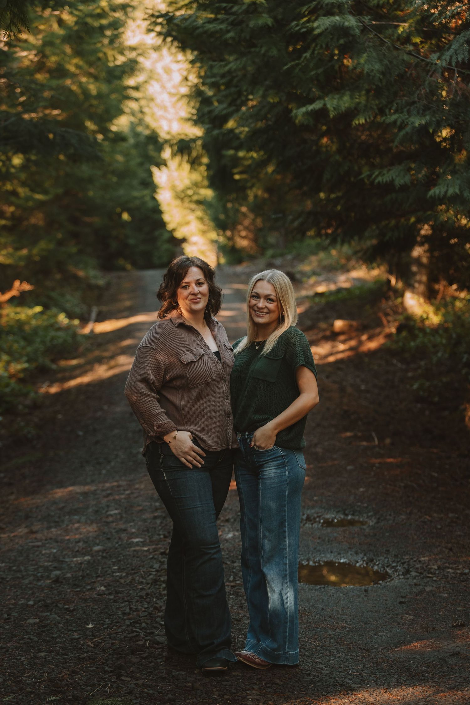 Two people share joyful laughter while standing close together on a dirt path surrounded by trees.
