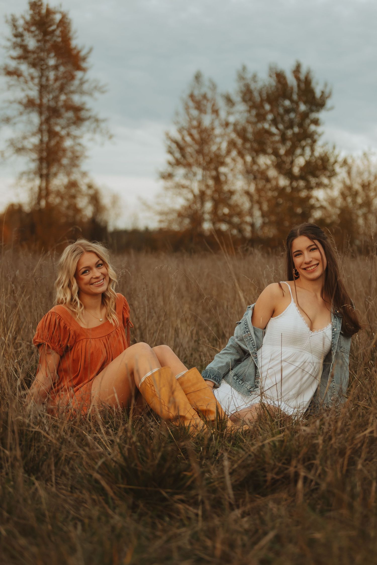 Friends lounging together in a rustic field wearing autumn-colored clothing at sunset.