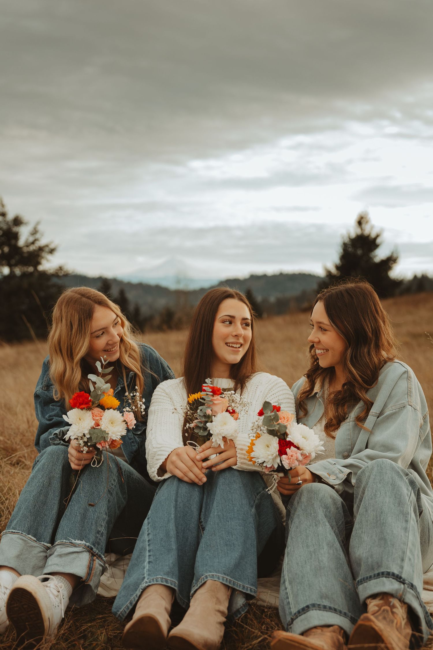 Group relaxing in casual denim outfits while holding colorful flower bouquets in a field.