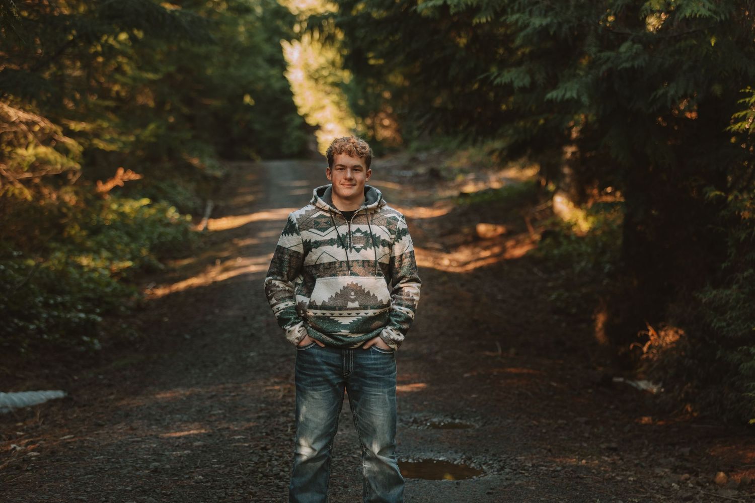 A person in a gray sweater and jeans walks down a scenic autumn forest path with golden sunlight filtering through trees.