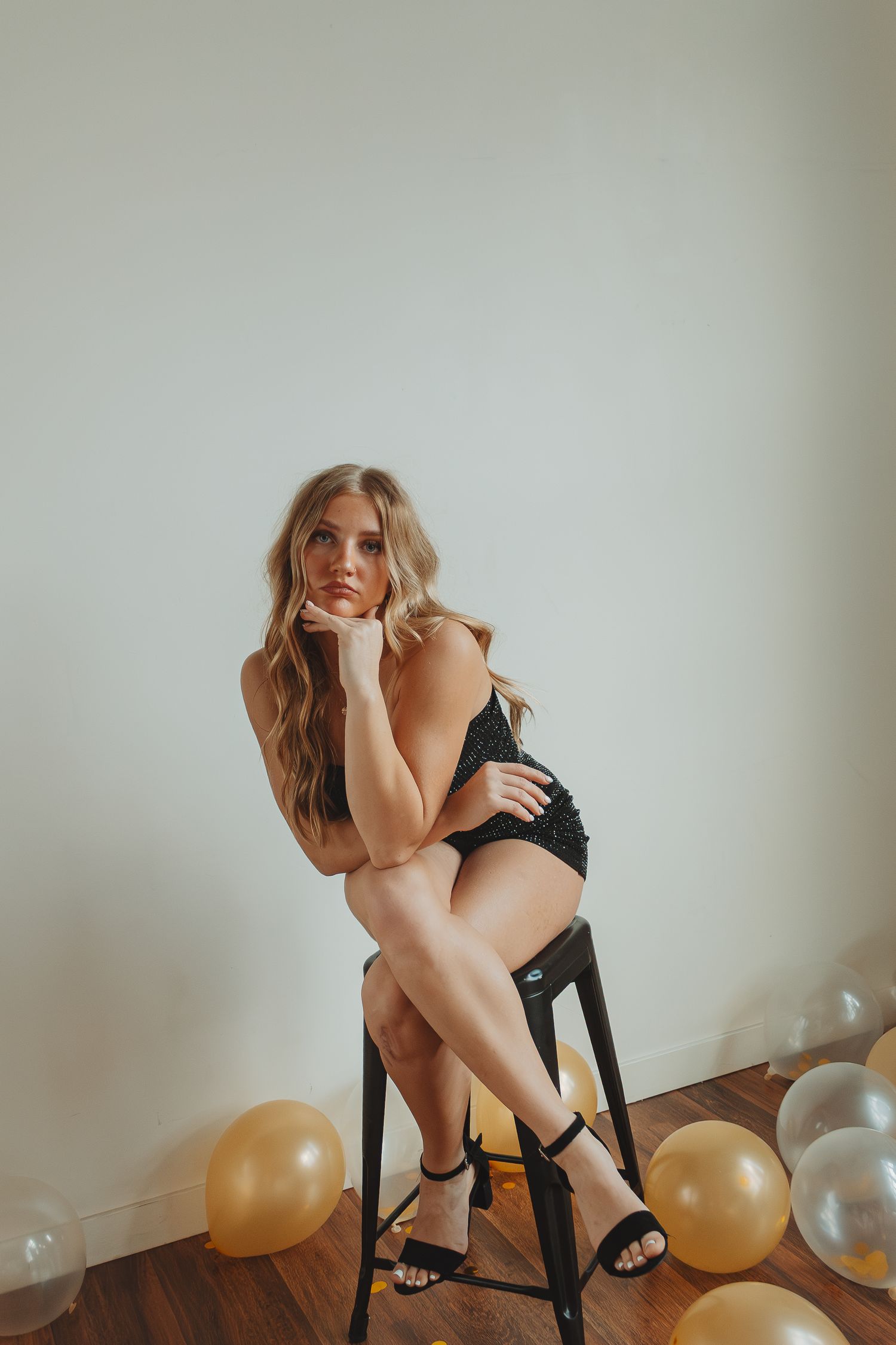 Artistic portrait session with gold and silver balloons against minimalist white wall backdrop.