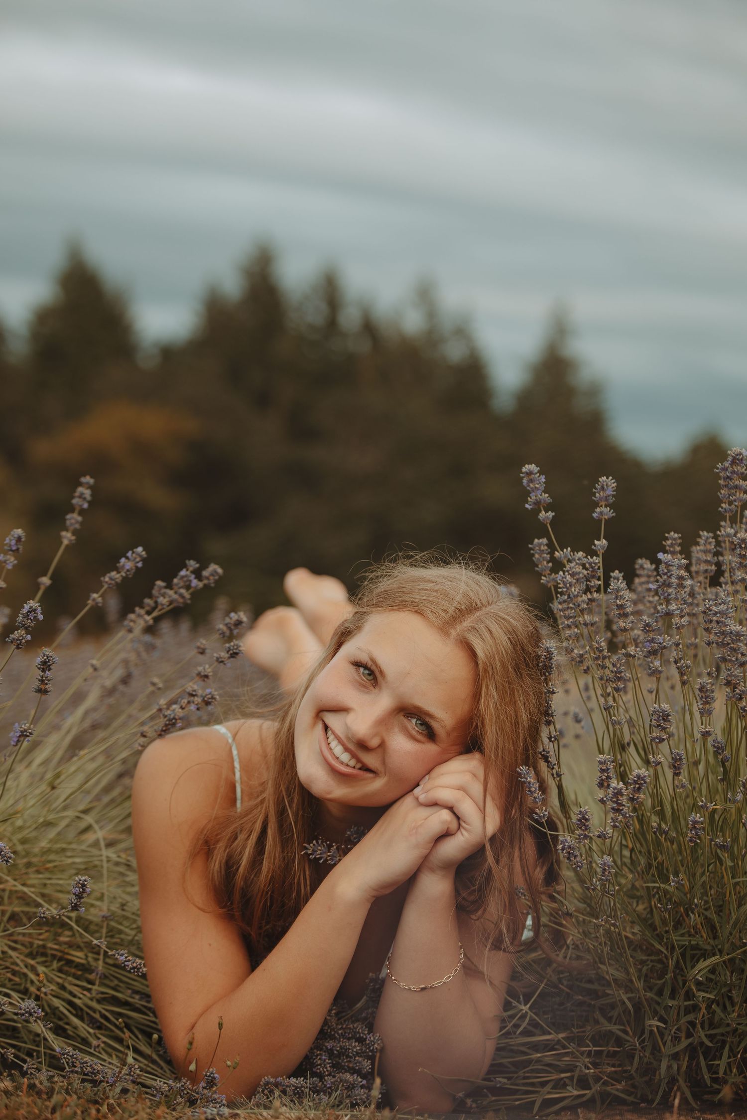 Candid portrait lying among blooming lavender plants with evergreen trees in background.