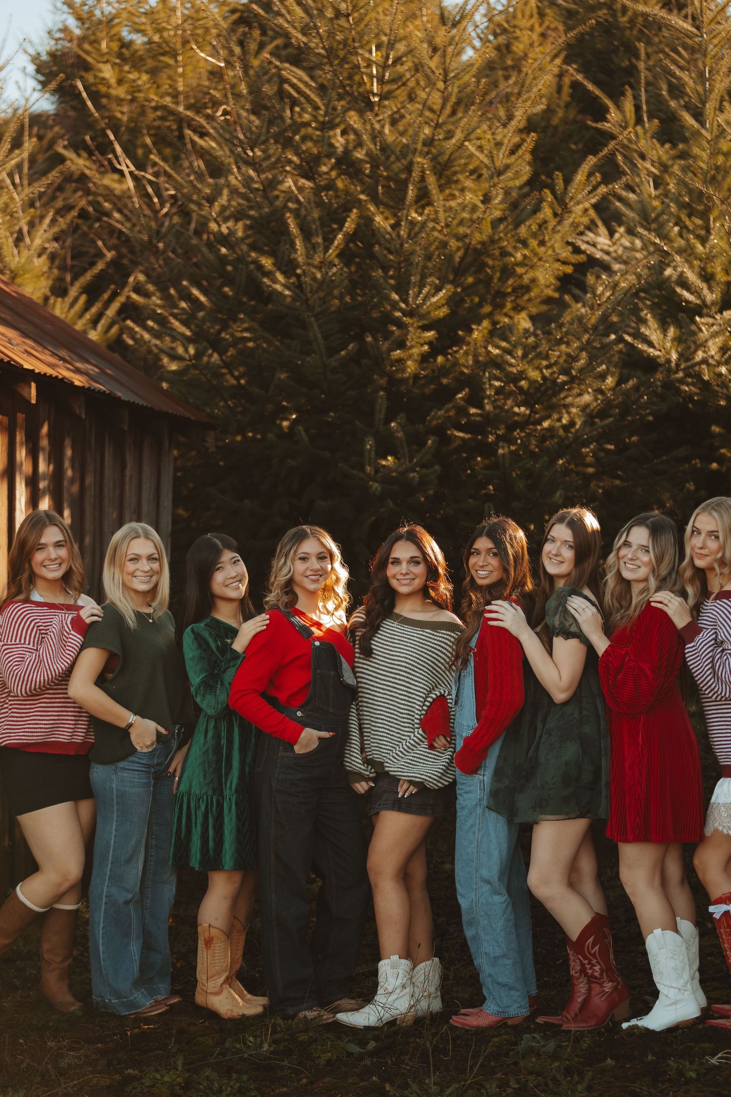Group photo of friends in festive winter outfits posing together by a rustic barn at sunset.