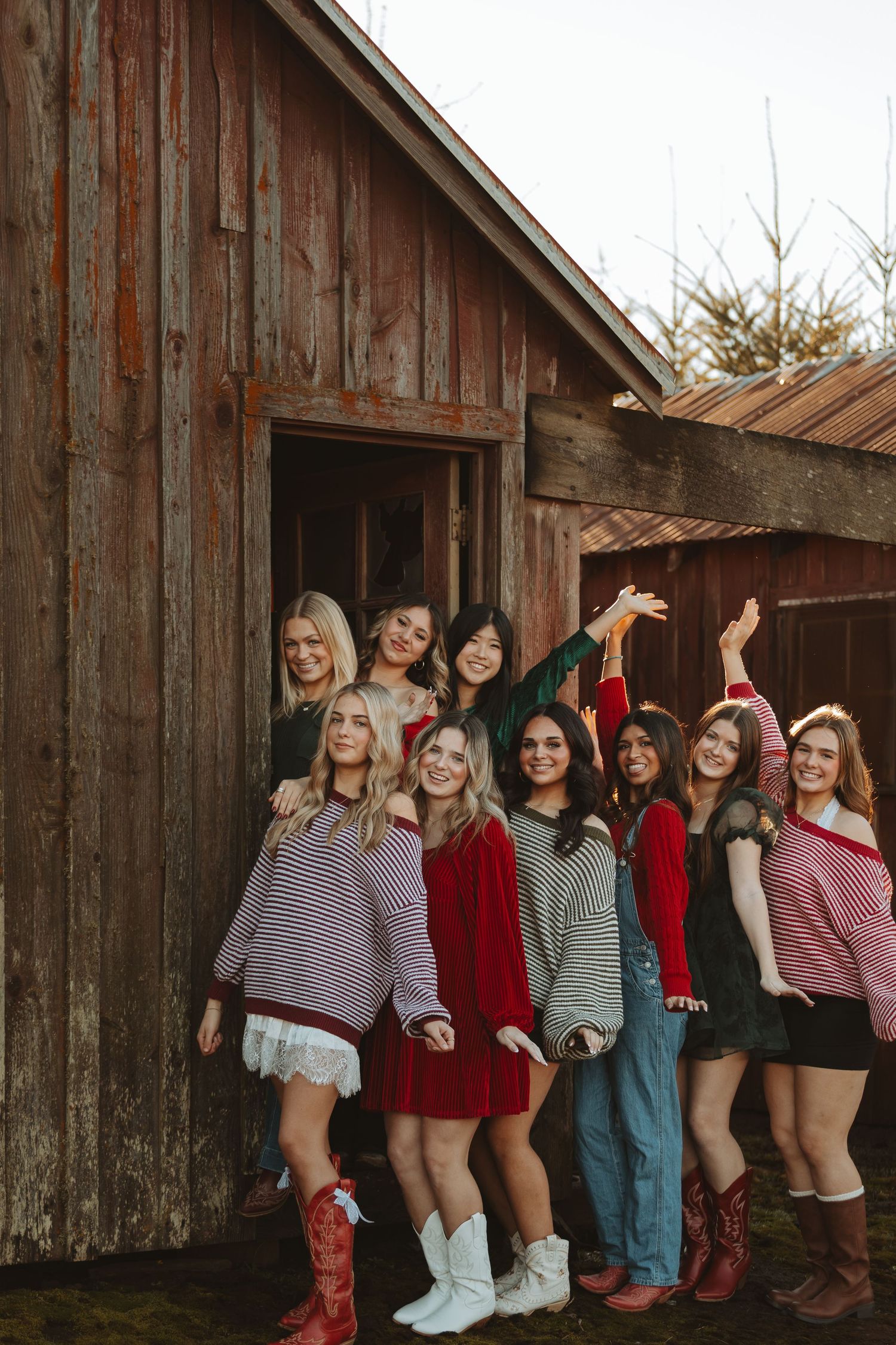 Friends in sweaters and boots having fun posing together against weathered barn wall.