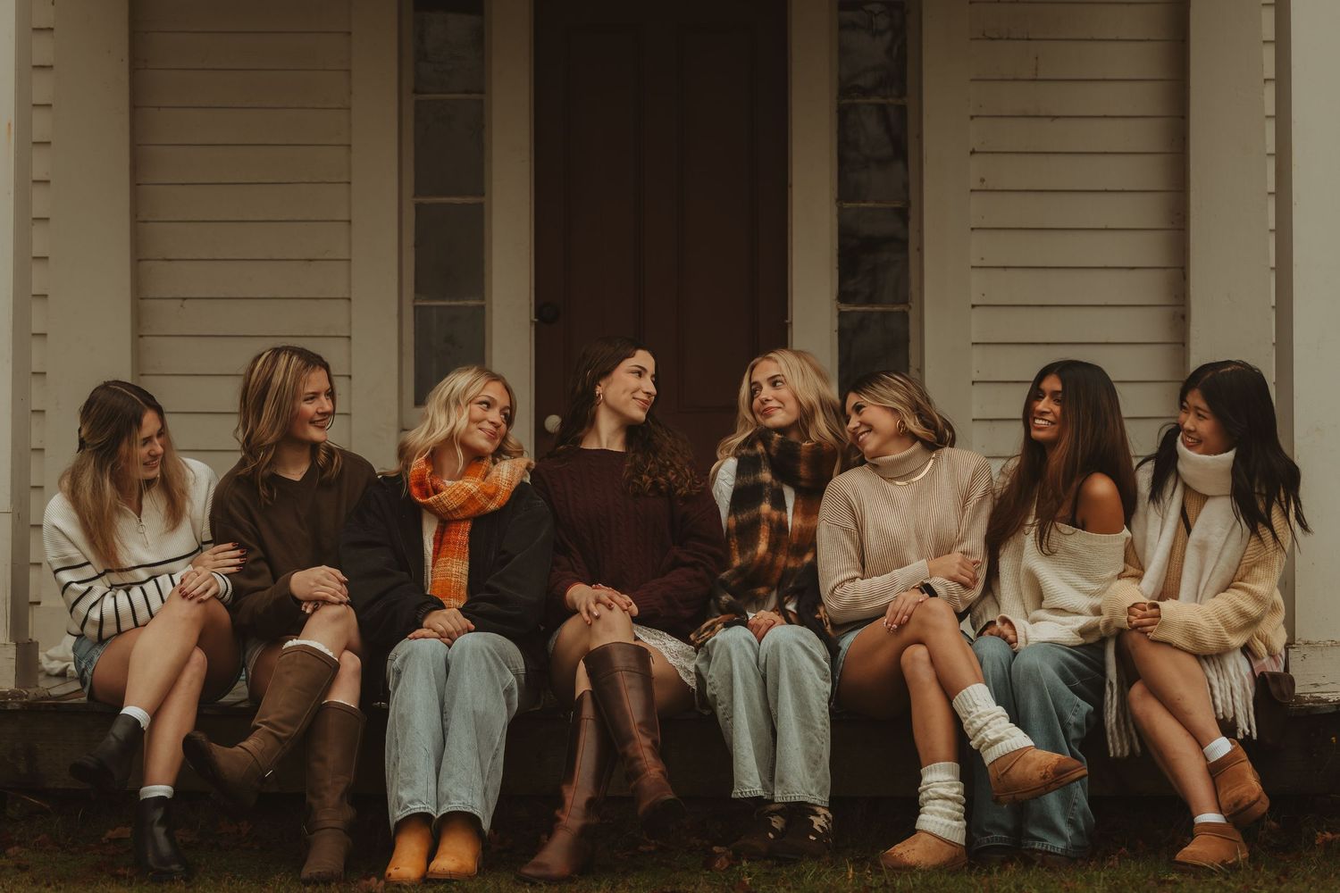 A group of friends sit together on wooden steps during a warm autumn evening in casual attire.