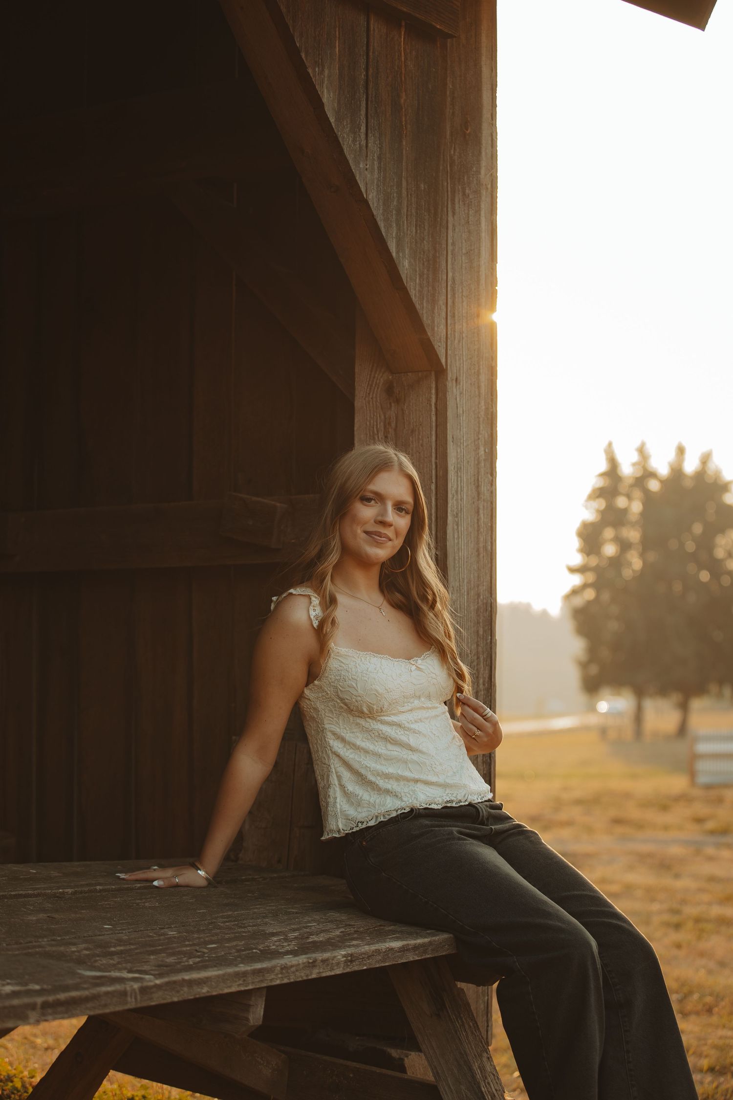 Woman in white top sits on rustic wooden porch at sunset with golden light streaming through the wooden beams.