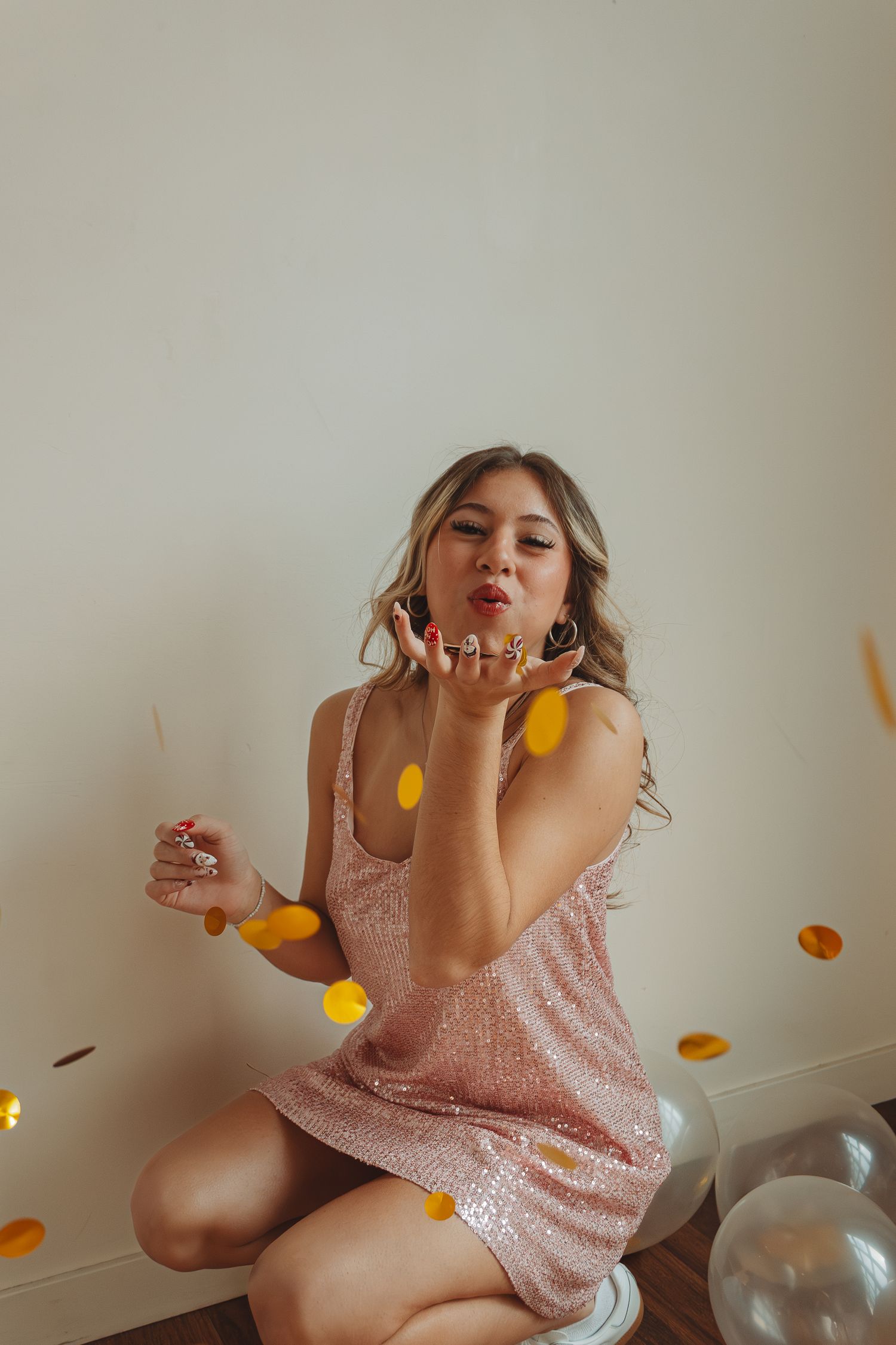 Playful scene with pink sequin dress and falling yellow flower petals against white wall.