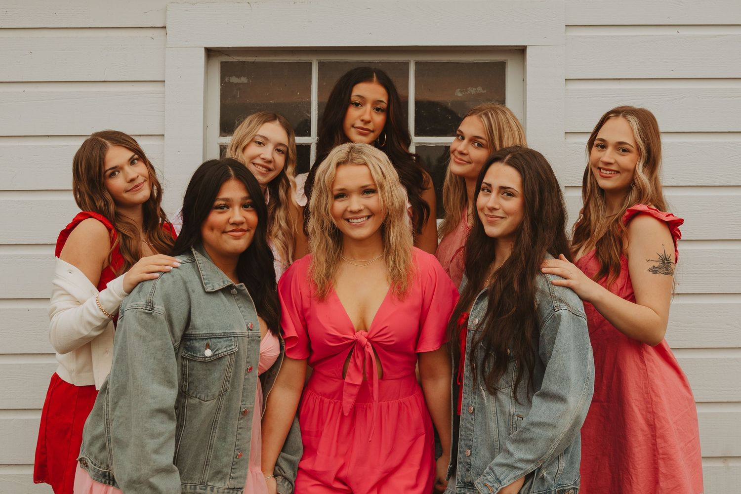 Group fashion photo with coordinated pink and red outfits against white building exterior.